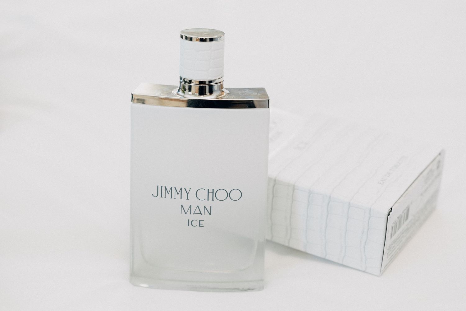 Jimmy Choo Man Ice EDT fragrance bottle in frosted glass with silver cap beside white striped box.