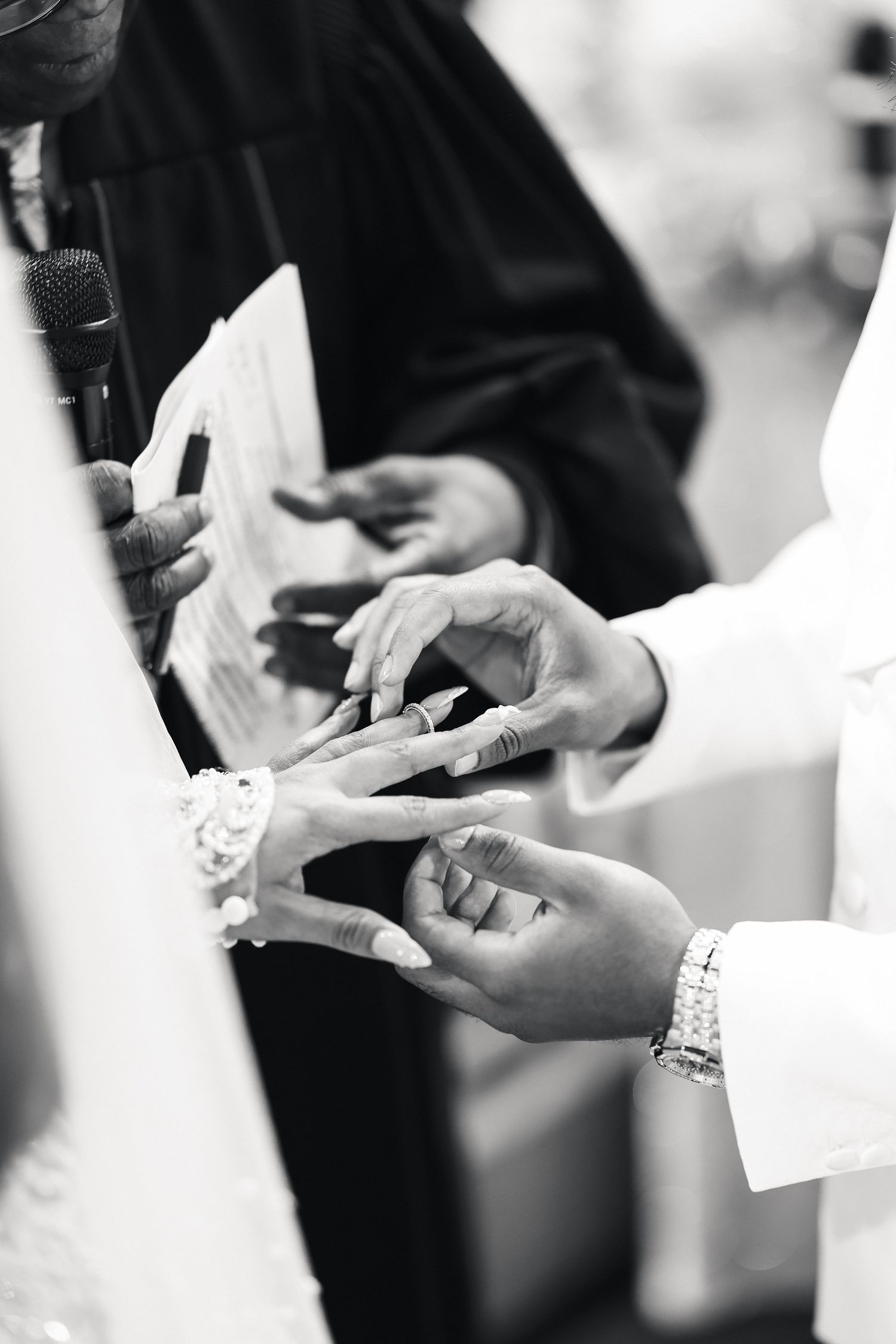 Close-up black and white photo of couple exchanging wedding rings during church ceremony.