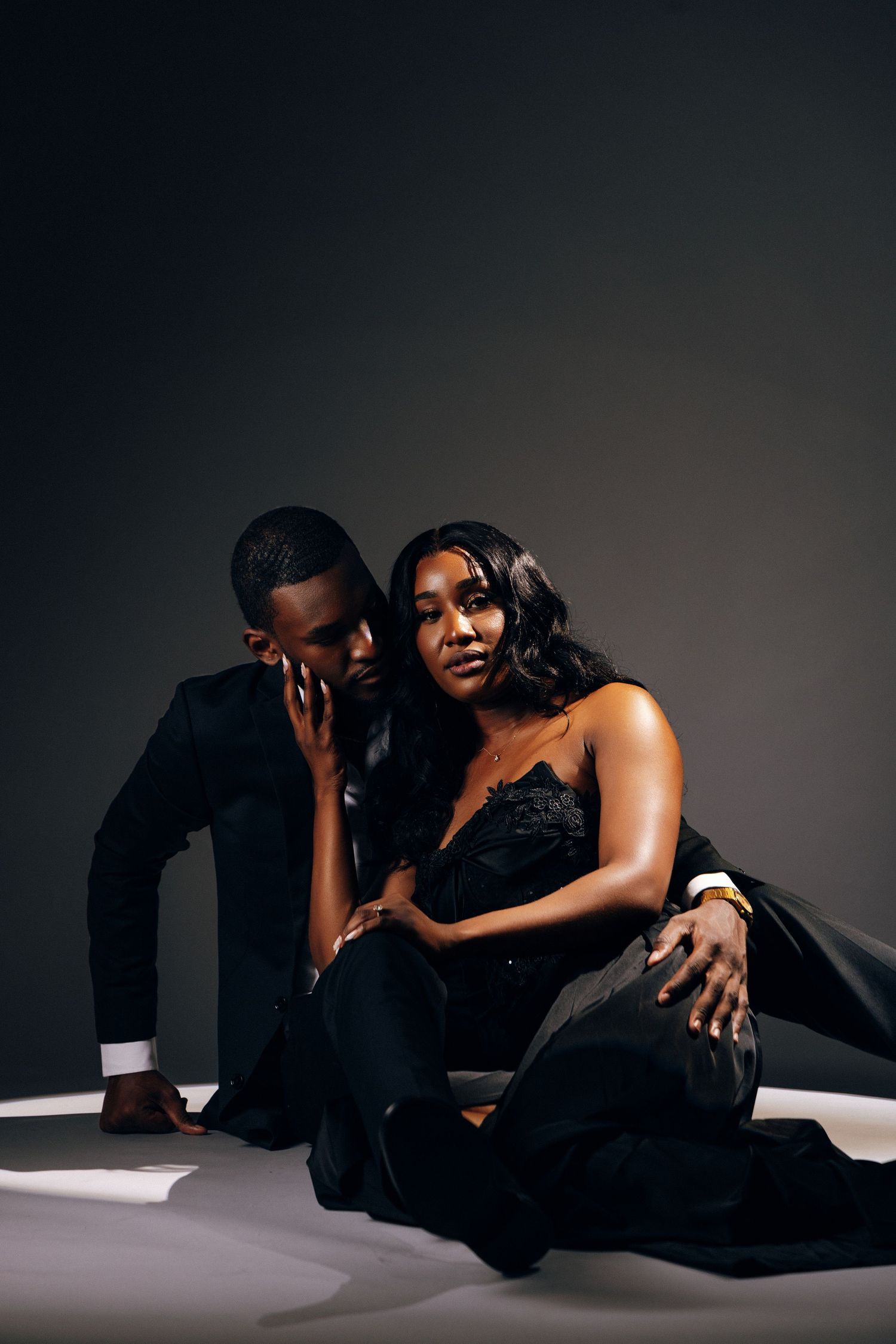 Elegant Black couple in formal attire posing together on dark background in a sophisticated studio portrait.