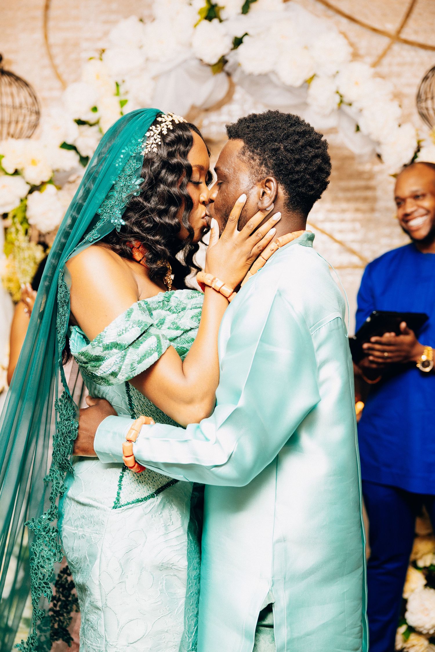Bride and groom share first kiss at altar in matching teal traditional African wedding attire.