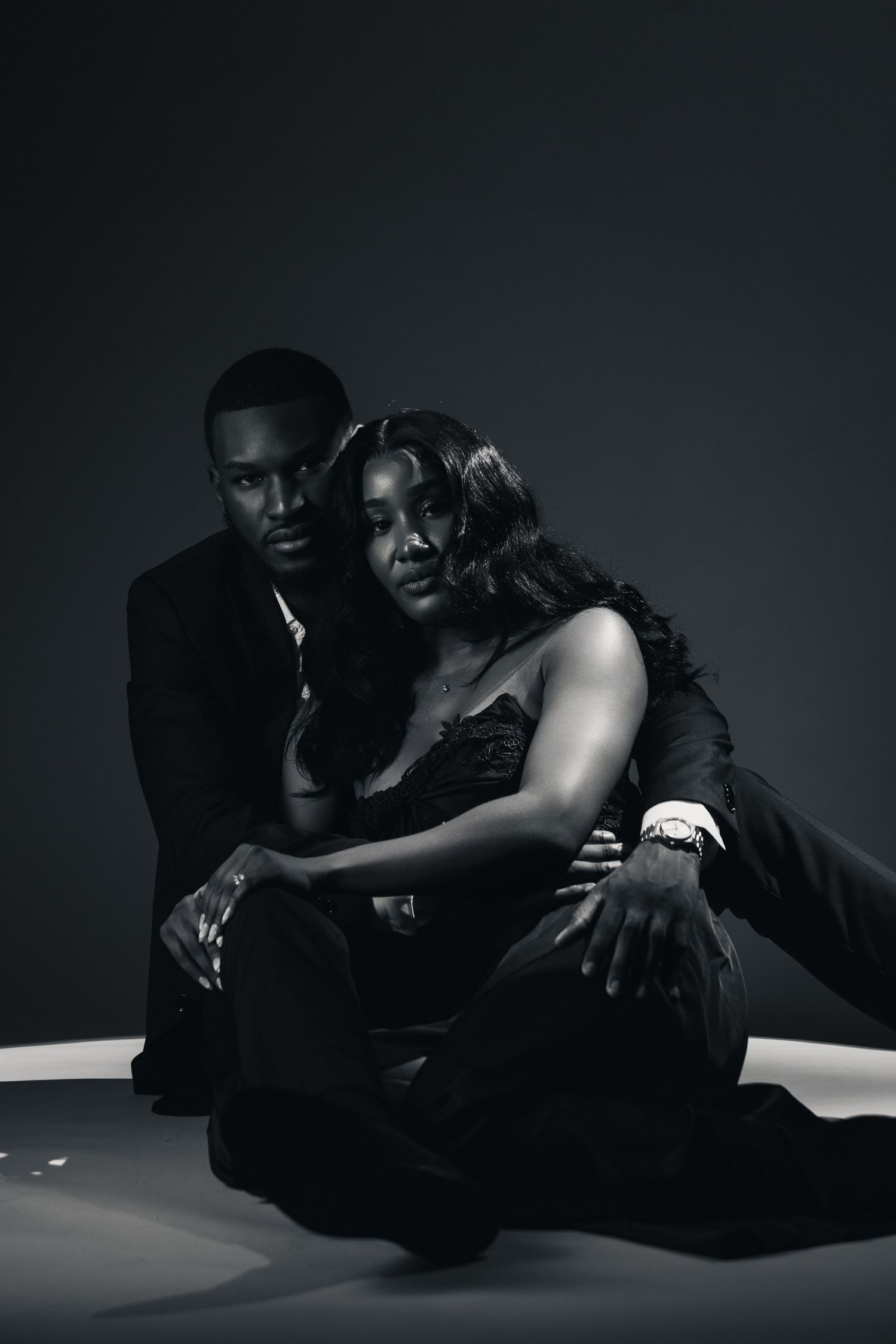 Black and white photo of an elegant couple sitting together, man in suit embracing woman in strapless dress.