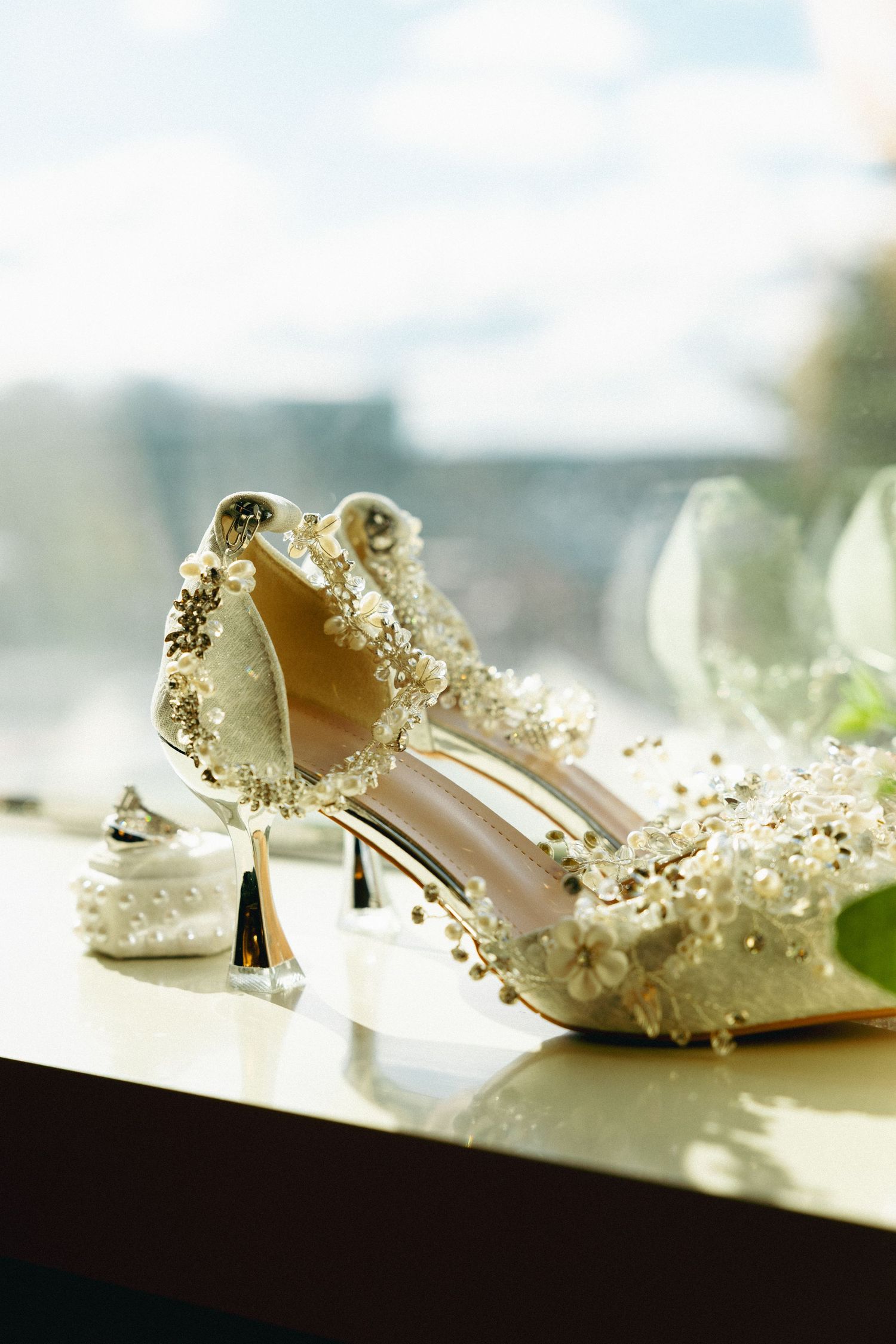 Elegant pearl-embellished bridal heels displayed on windowsill with soft natural light.