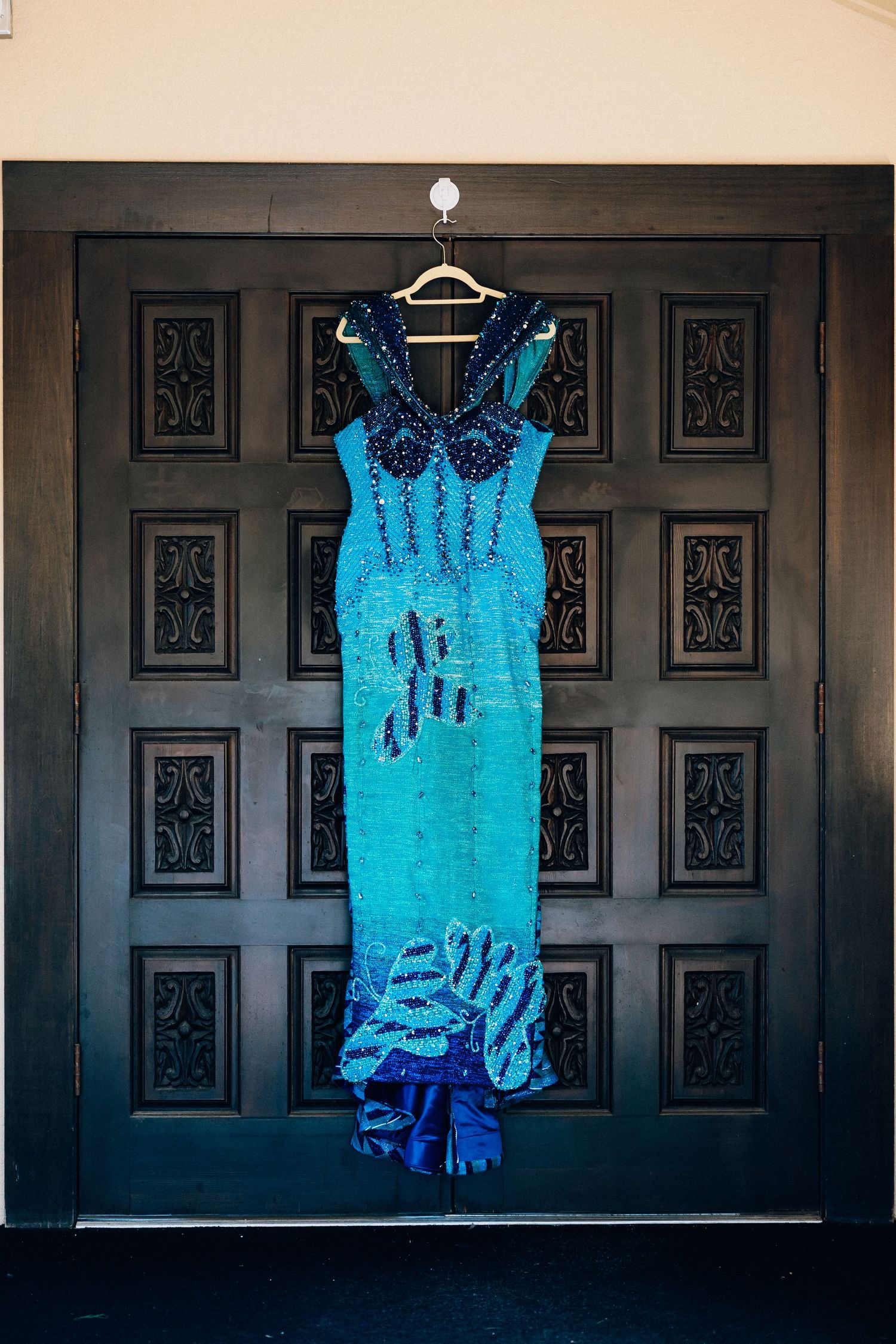 Stunning teal sequined Nigerian traditional wedding dress hanging on dark wooden door.