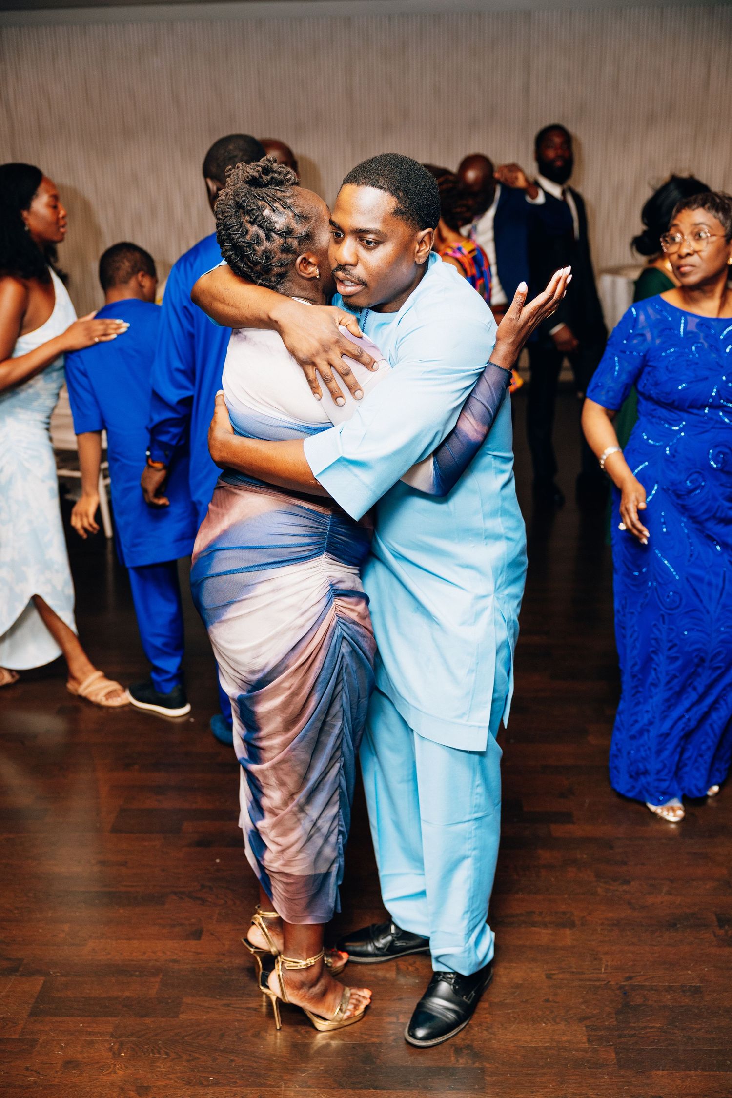 Couple sharing an intimate slow dance embrace at a formal wedding reception with guests in blue attire.
