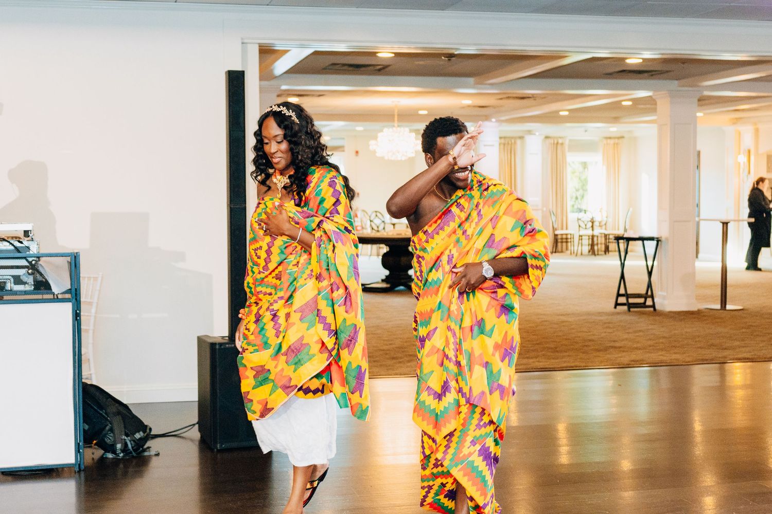 Two people dancing in vibrant Kente cloth attire at an elegant indoor event celebration.