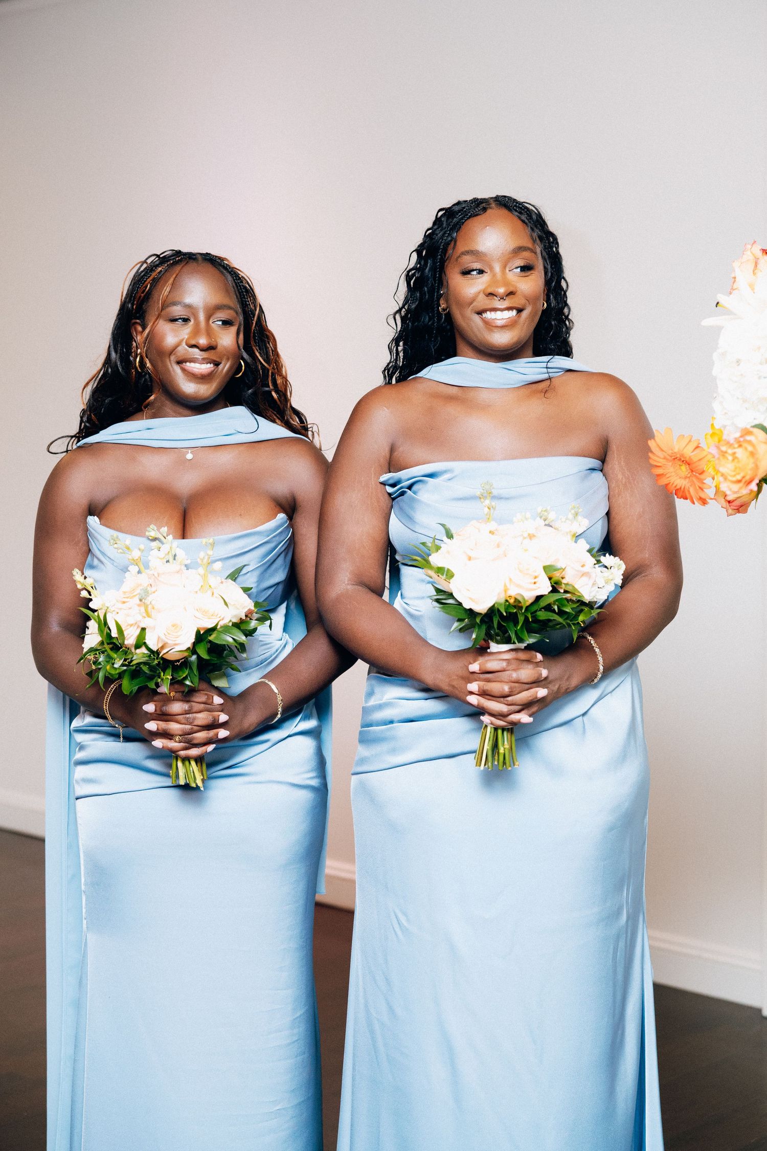 Two bridesmaids in light blue halter gowns holding white and peach bouquets pose at wedding.