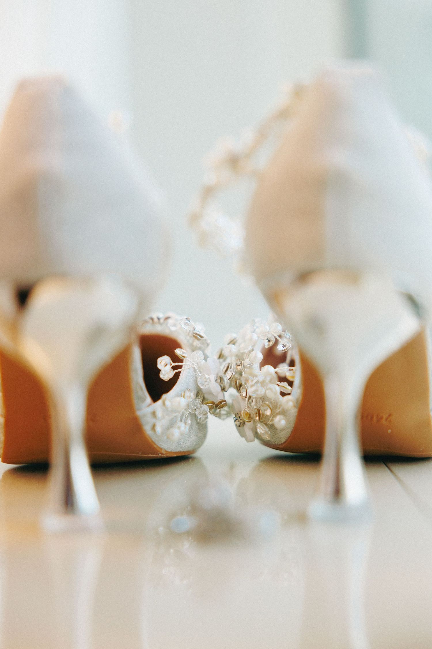 Close-up of white pearl-embellished bridal heels with stiletto backs reflecting on a glossy surface.