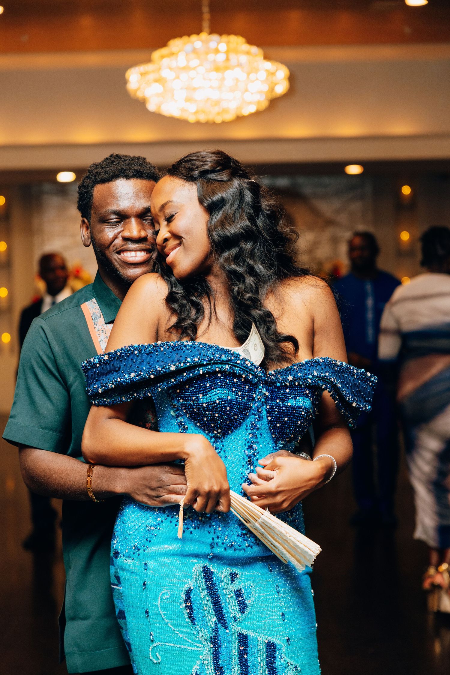Happy couple embraces on dance floor, bride in blue beaded off-shoulder gown at wedding reception.