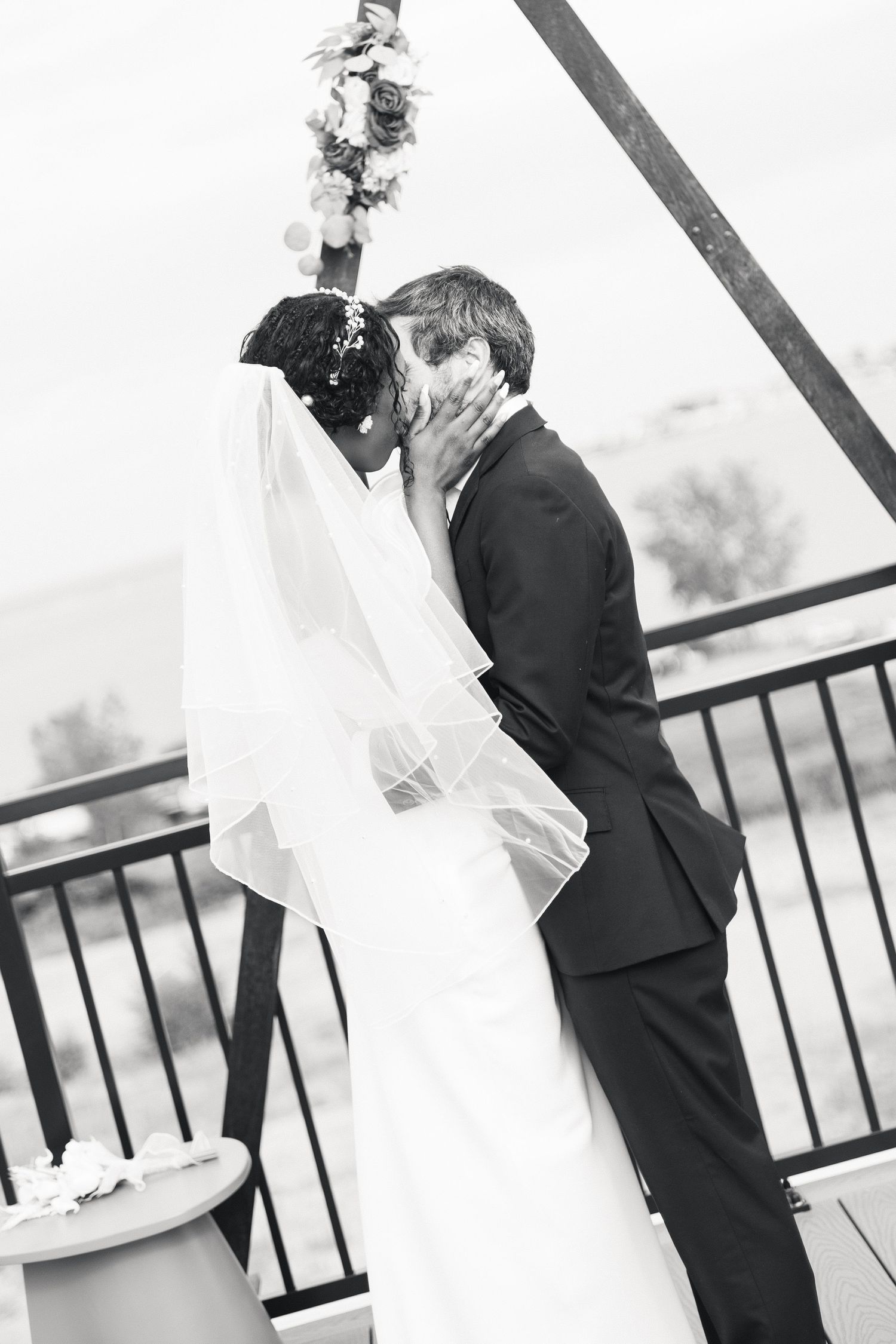 Black and white photo of a bride and groom sharing their first kiss at the altar during their wedding ceremony.