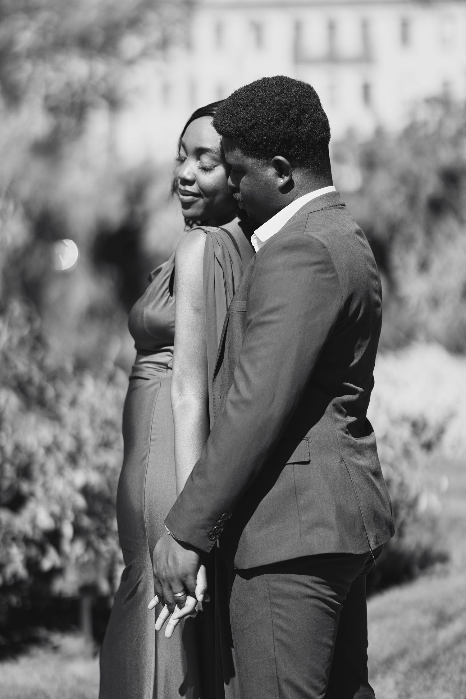 Black and white photo of an elegant couple in formal wear sharing a tender moment outdoors.