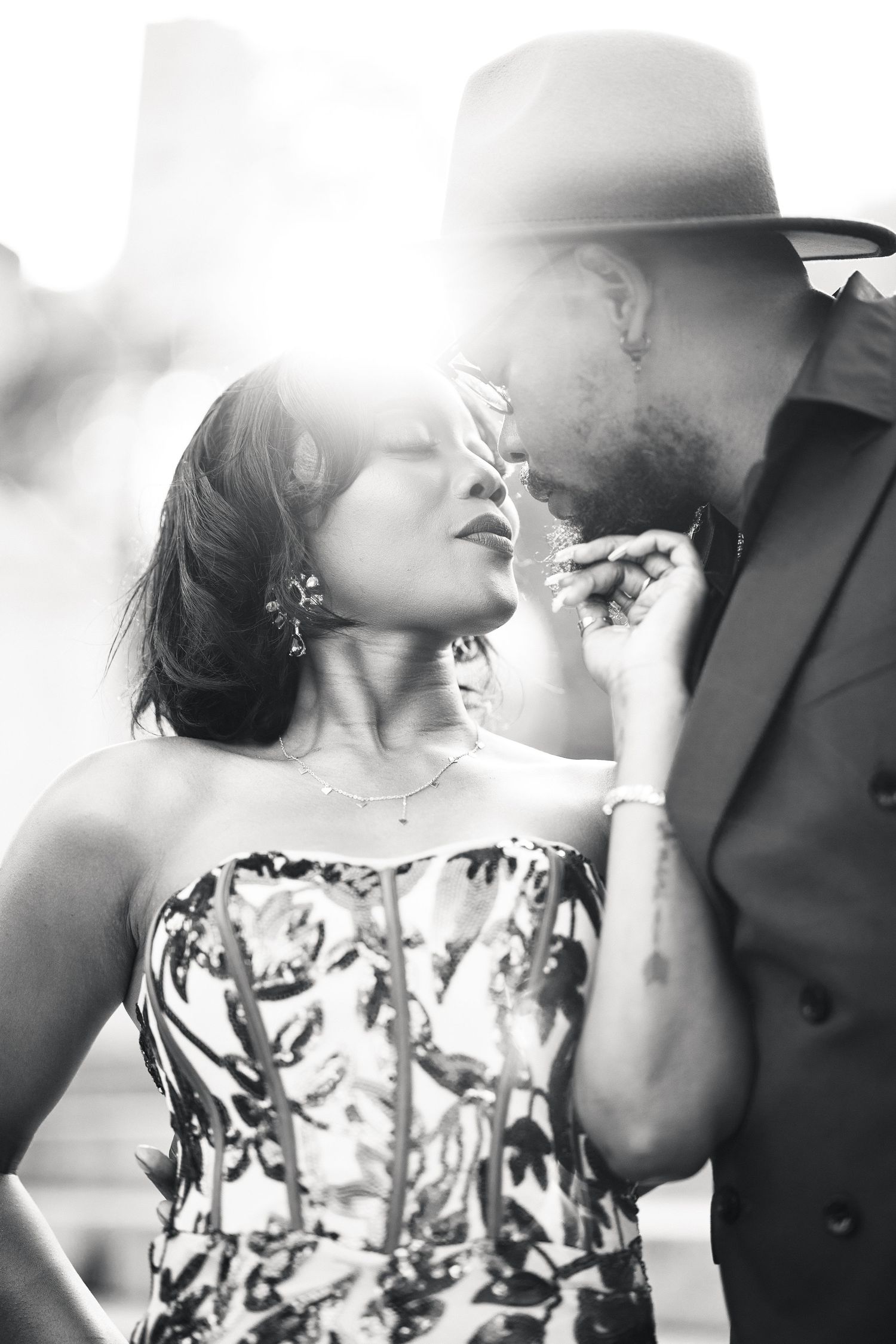 Black and white photo of an elegant couple sharing an intimate moment, backlit by sunlight.