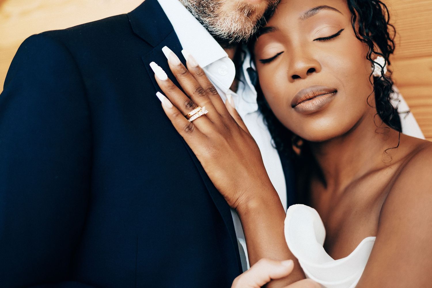 African American bride with engagement ring rests her head on groom's shoulder in an intimate wedding embrace.