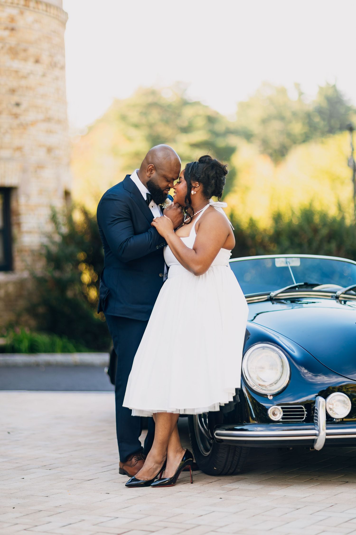 Bride and groom sharing a romantic moment leaning against a classic blue vintage car outdoors.