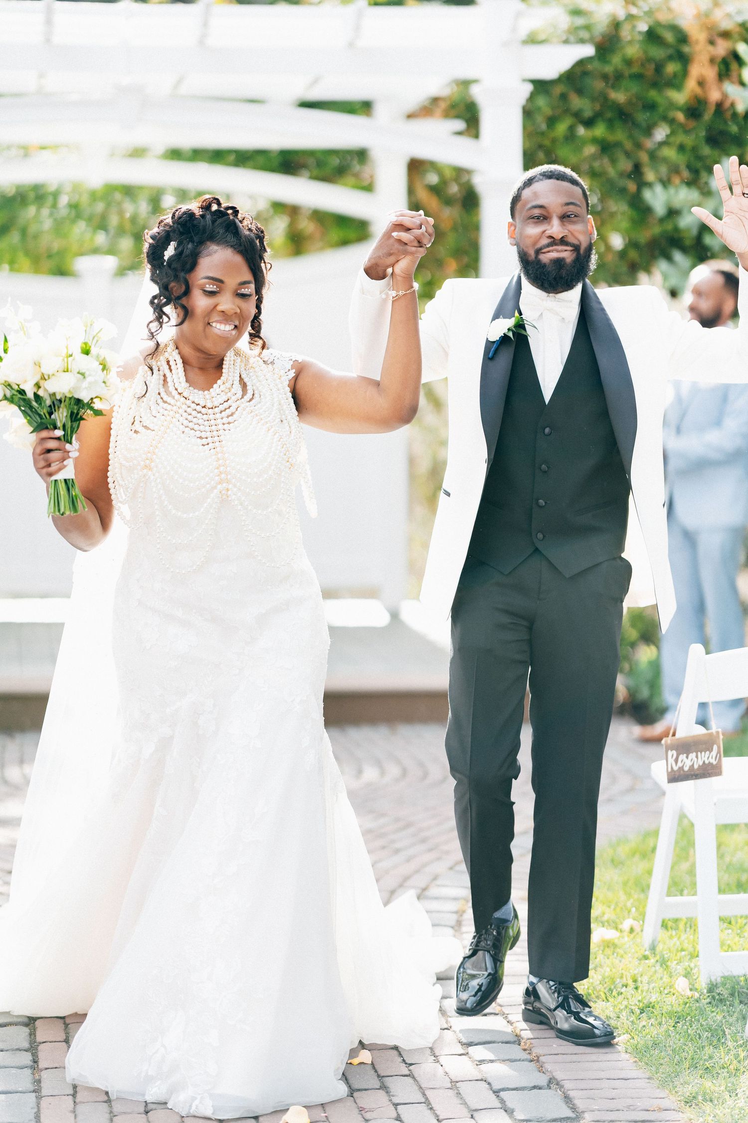 A joyful bride and groom celebrate after their wedding ceremony, raising hands in triumph on a brick pathway.