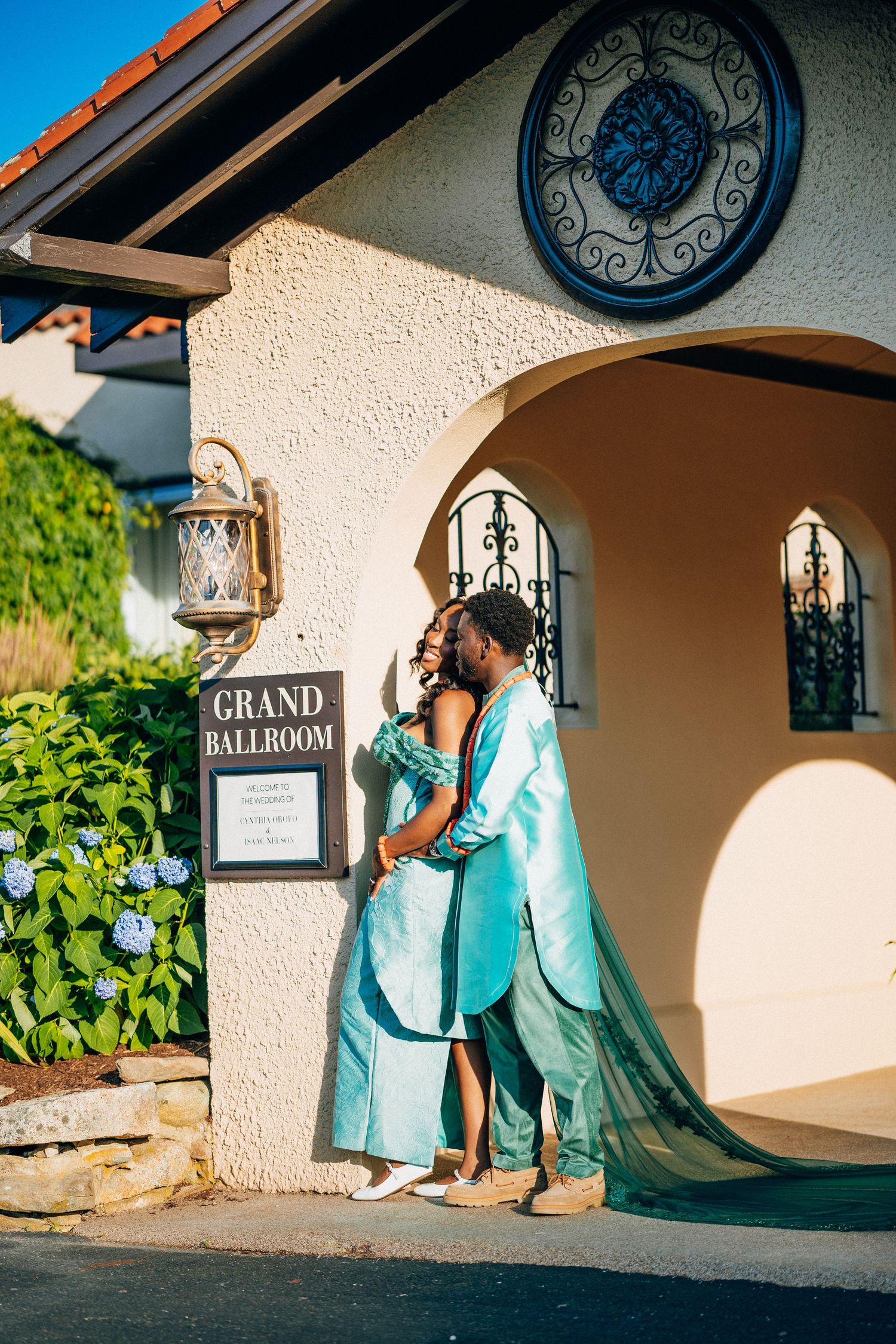 Couple in teal wedding attire embracing at Grand Ballroom entrance with hydrangeas nearby.
