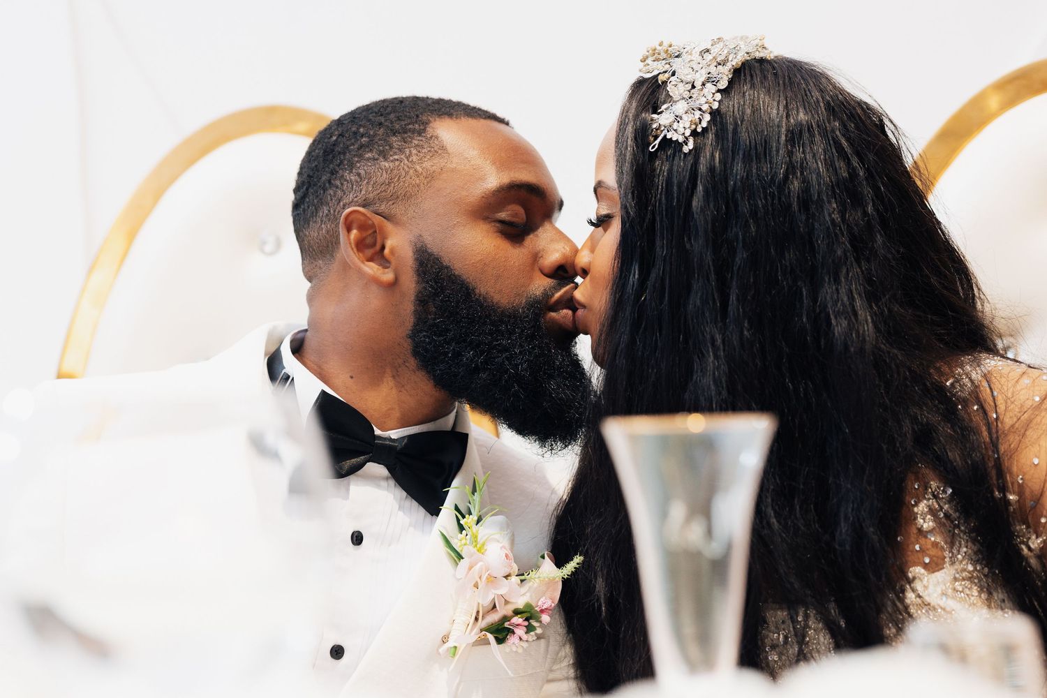 A bride and groom share a romantic kiss at their wedding reception, dressed in elegant formal attire.