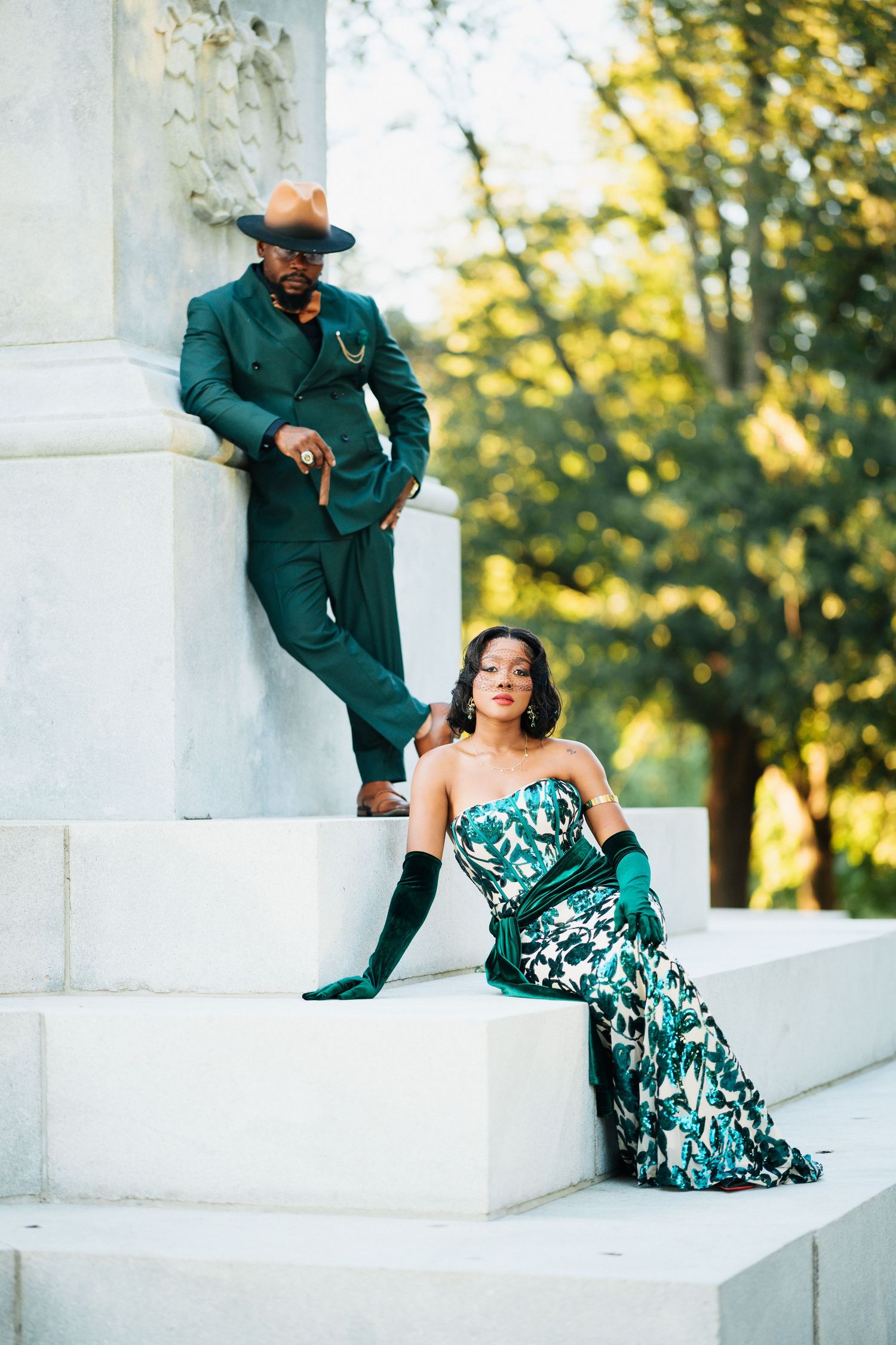 Fashionable Black couple in emerald green attire posing on white stone monument steps.