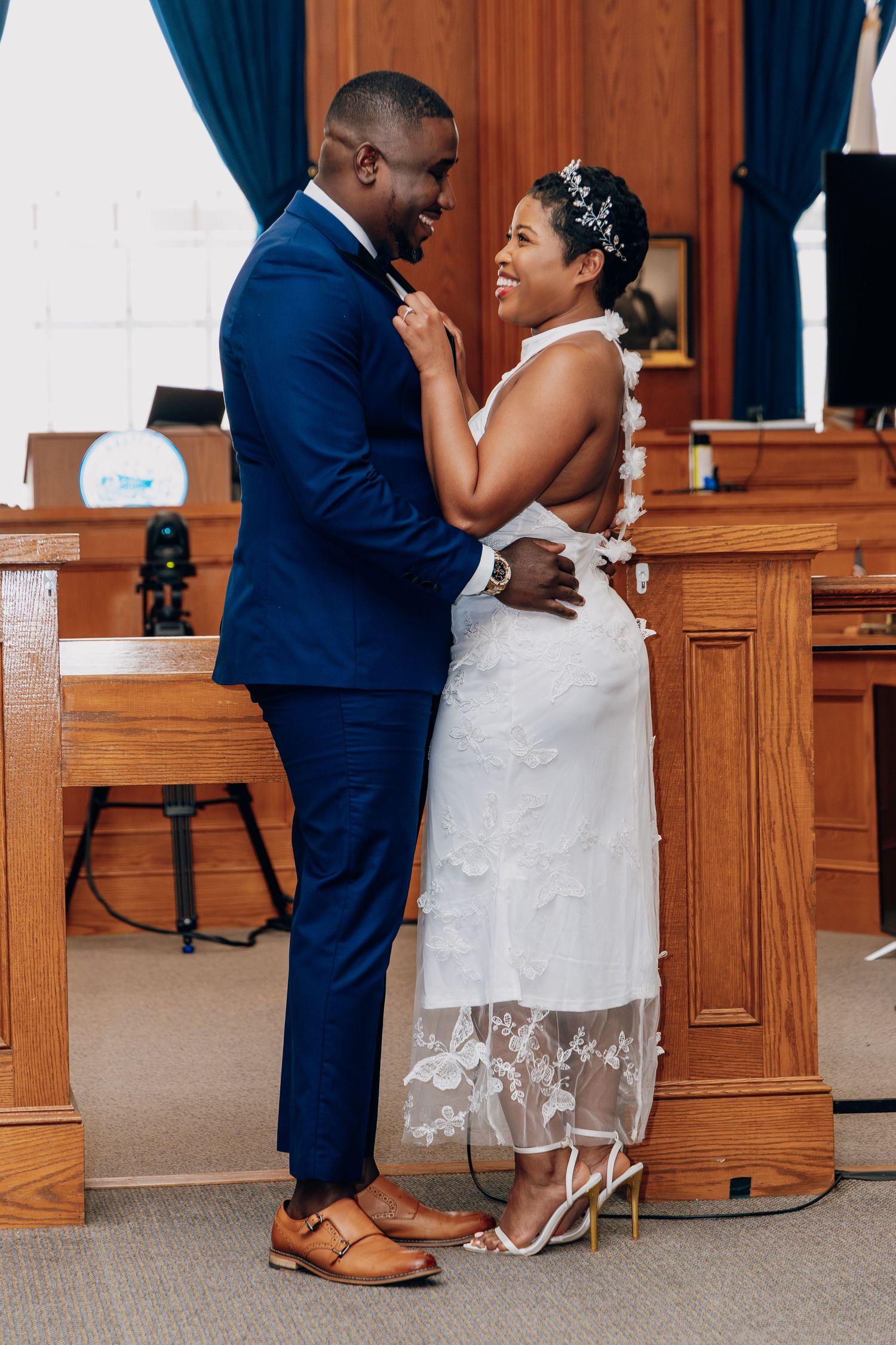 A joyful Black couple in wedding attire embrace and laugh together inside a courthouse during their civil ceremony.
