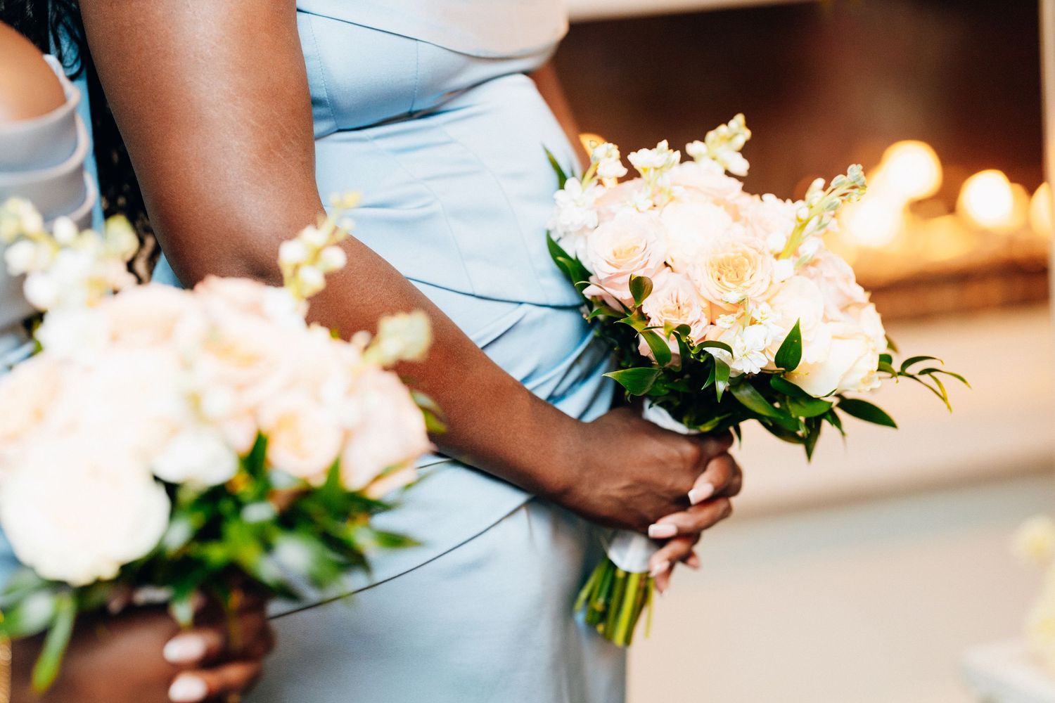 Bridesmaids in light blue dresses holding elegant white and blush floral bouquets at a wedding ceremony.