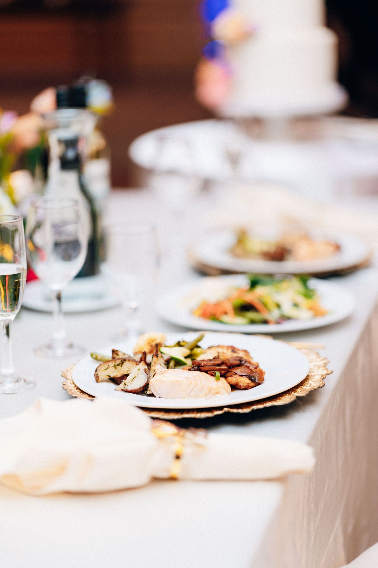 Elegant wedding reception dinner plate with chicken and mushrooms on gold-rimmed charger plate.