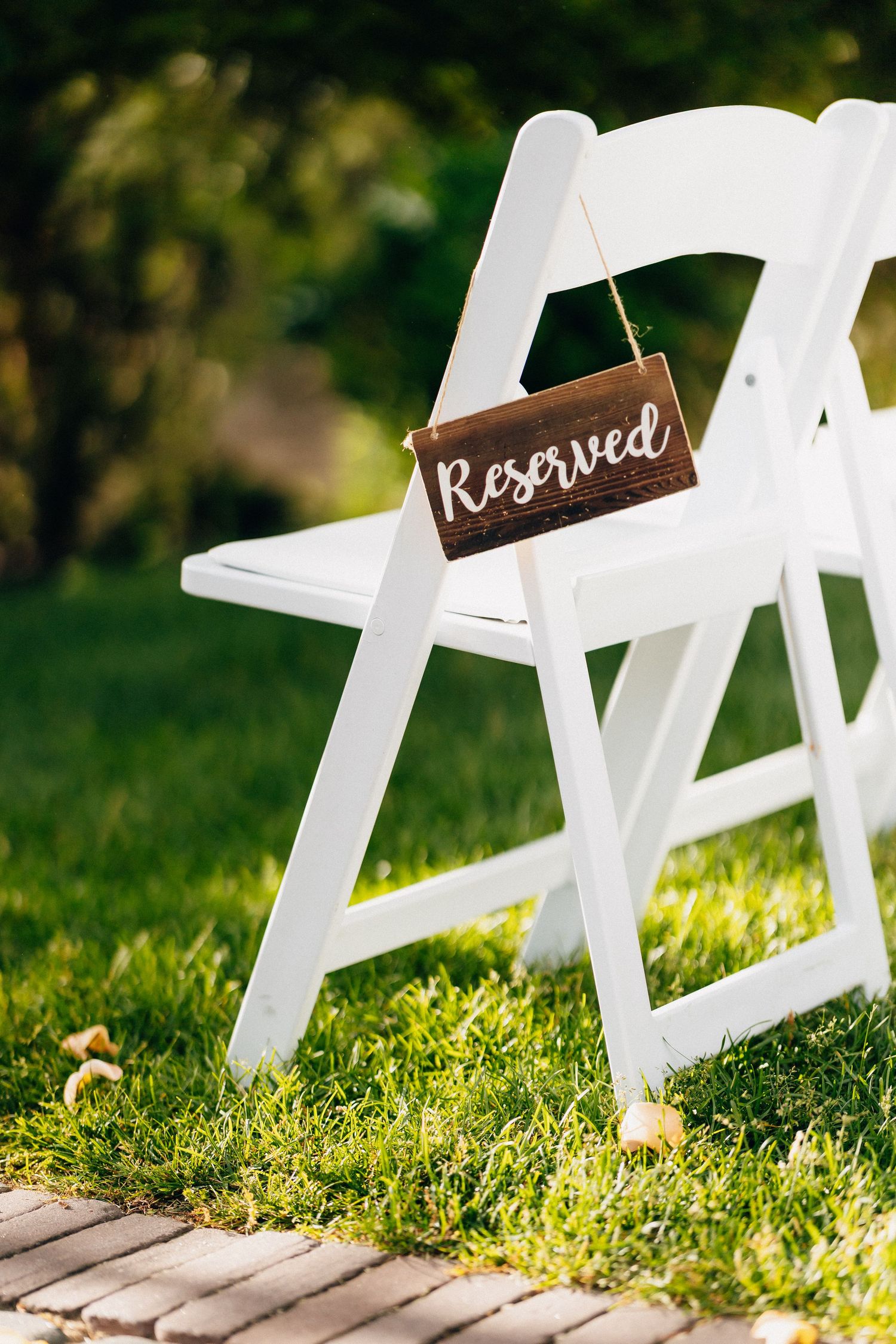 White wooden folding chair with rustic wooden Reserved sign hanging on it on green grass.