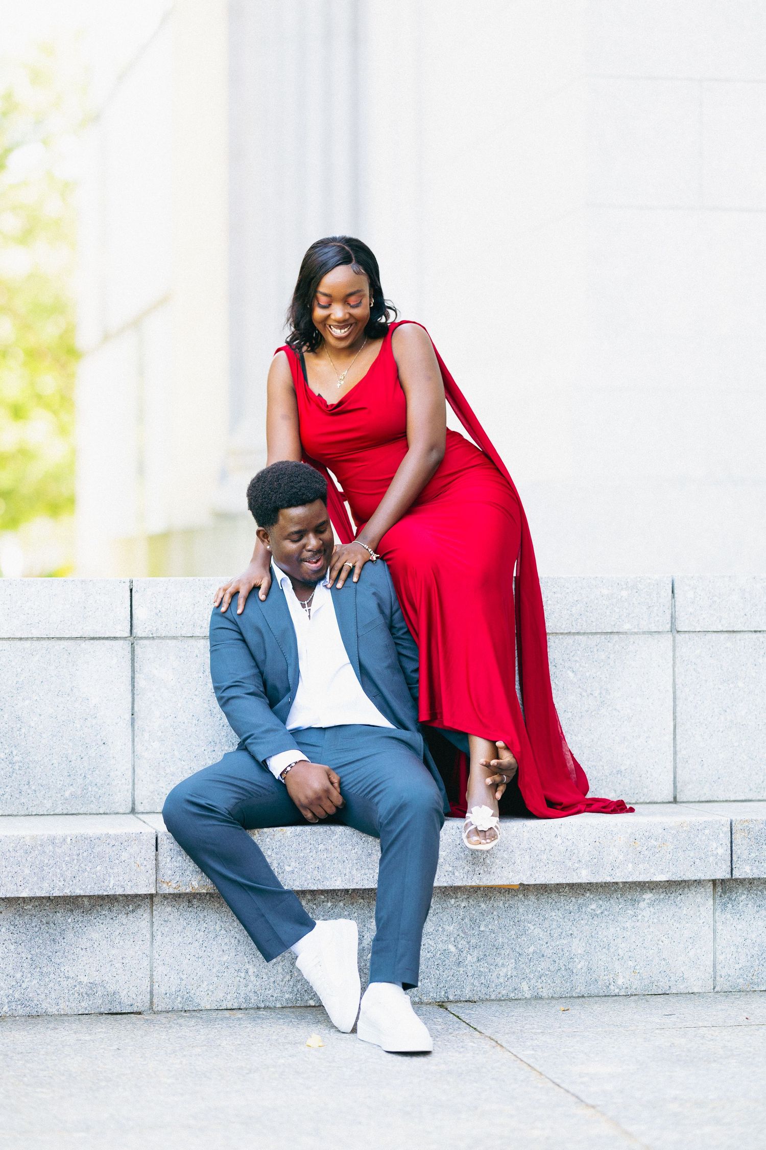 Couple laughing on stone steps, woman in red cape dress standing behind seated man.