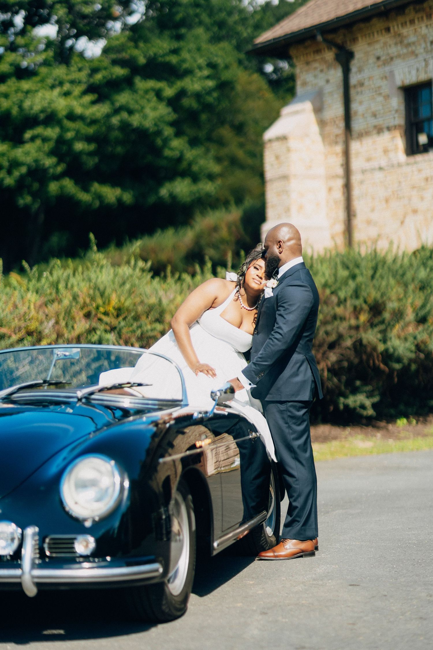 Bride and groom sharing a romantic moment beside a vintage black Porsche at an outdoor venue.