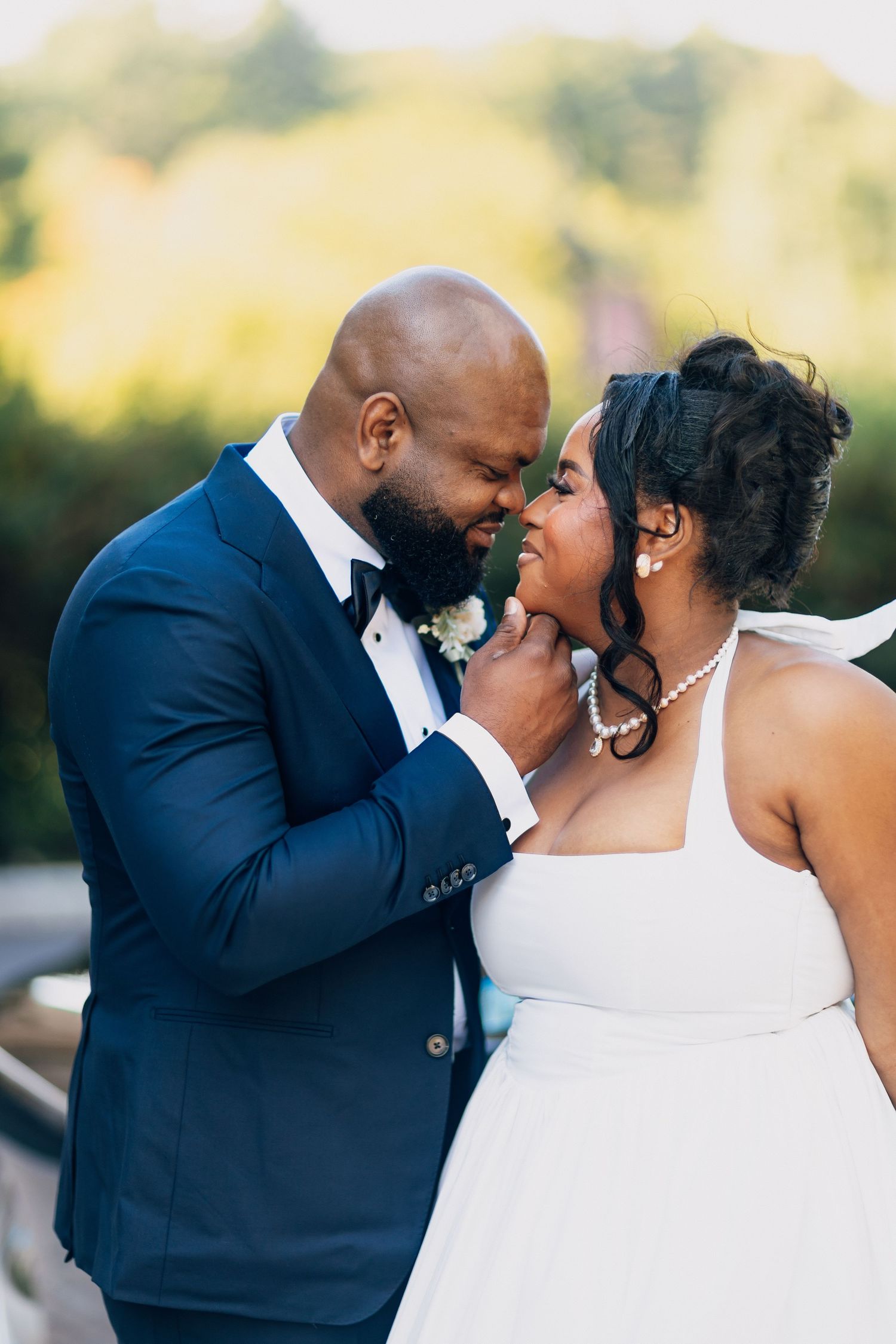 A groom gently holds his bride's chin as they share an intimate moment outdoors.