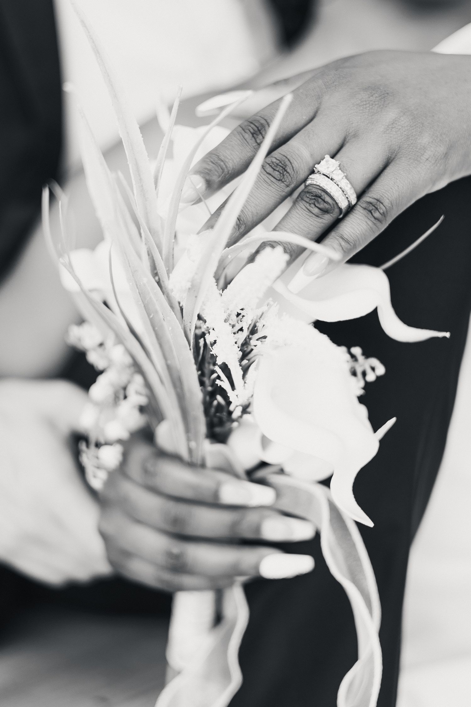Black and white photo of hands holding a wedding bouquet with a diamond ring visible on the bride's finger.