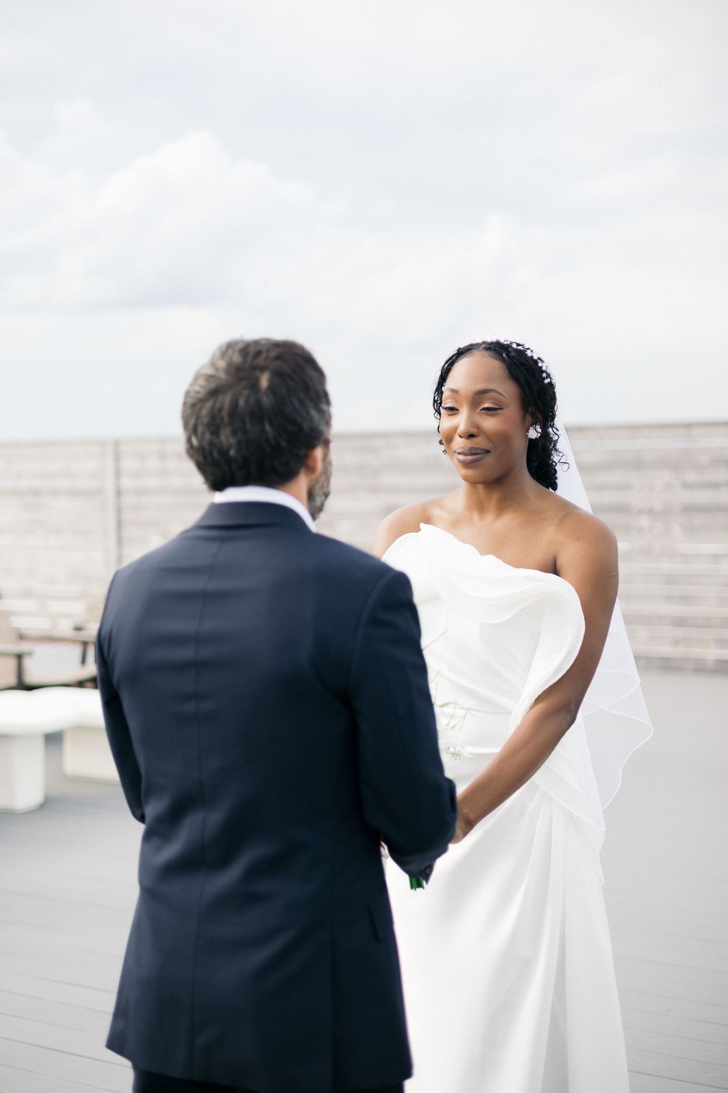 Bride in white gown holds hands with groom in navy suit during outdoor wedding ceremony.