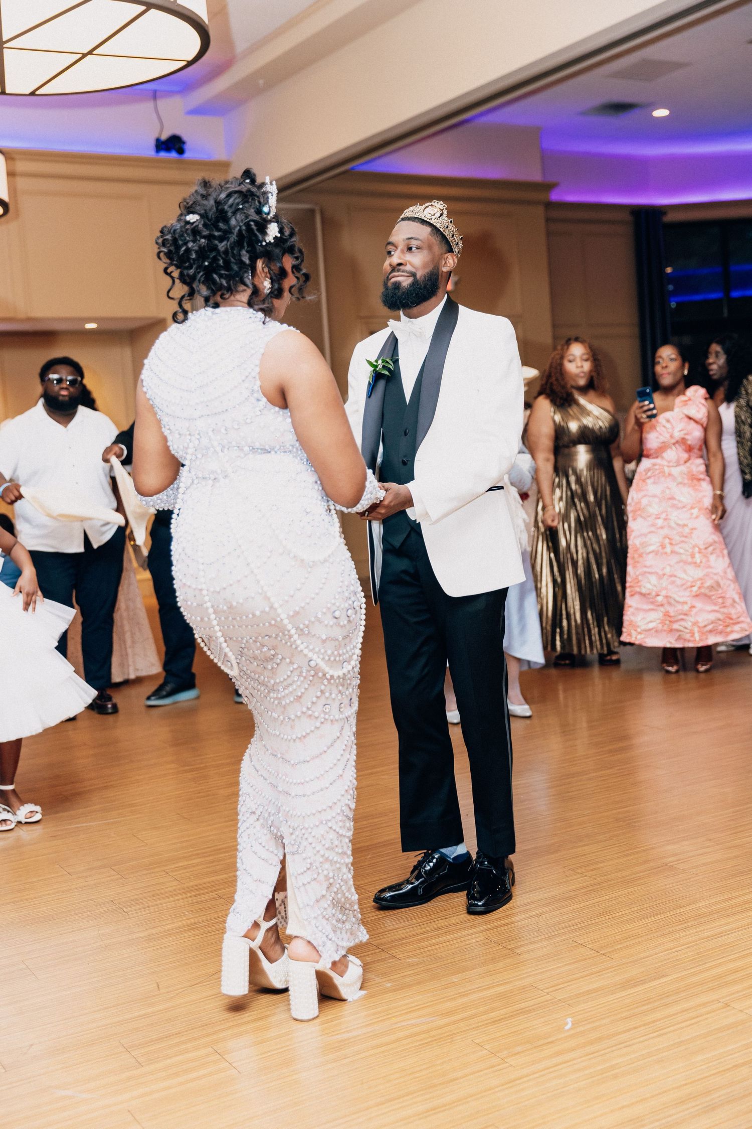 Bride and groom share their first dance at wedding reception, guests watching in elegant ballroom with purple lighting.