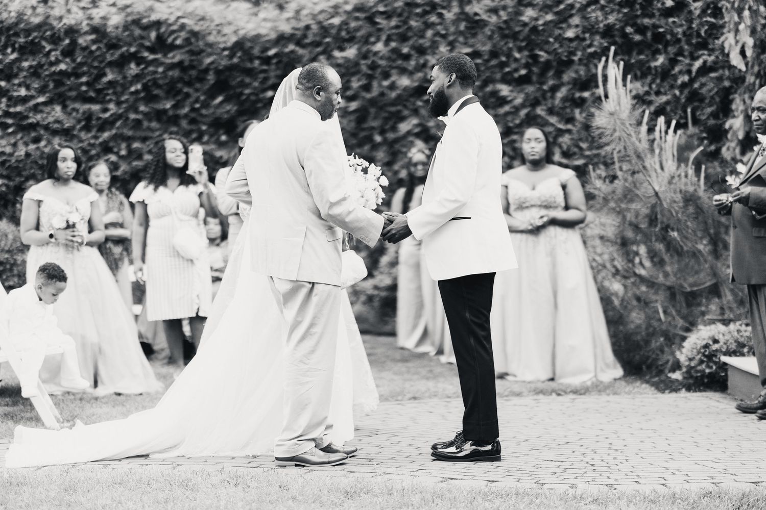 Black and white outdoor wedding ceremony with bride, groom, and bridesmaids in elegant attire.