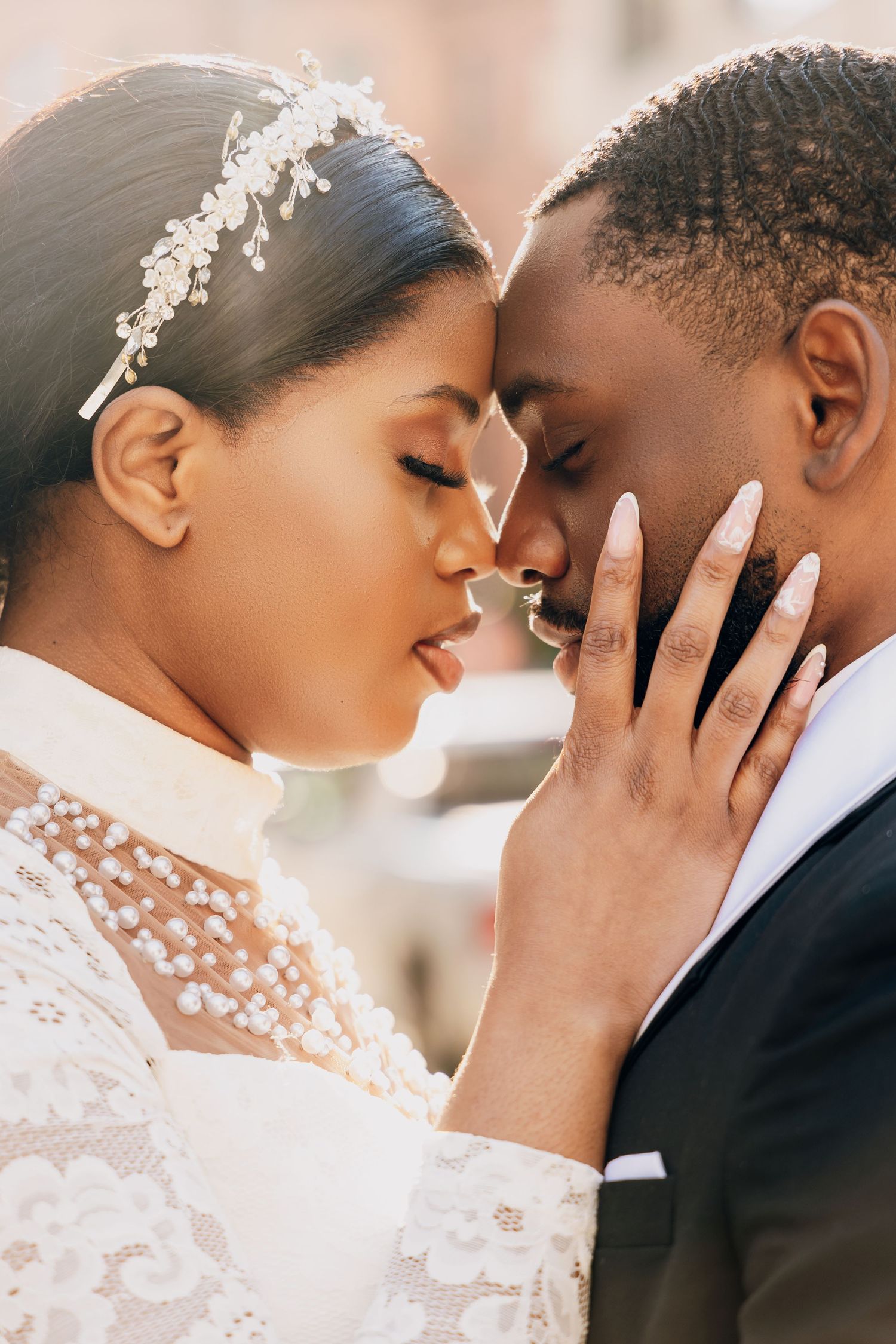 A Black bride and groom share an intimate moment, touching foreheads, as she gently cups his face on their wedding day.