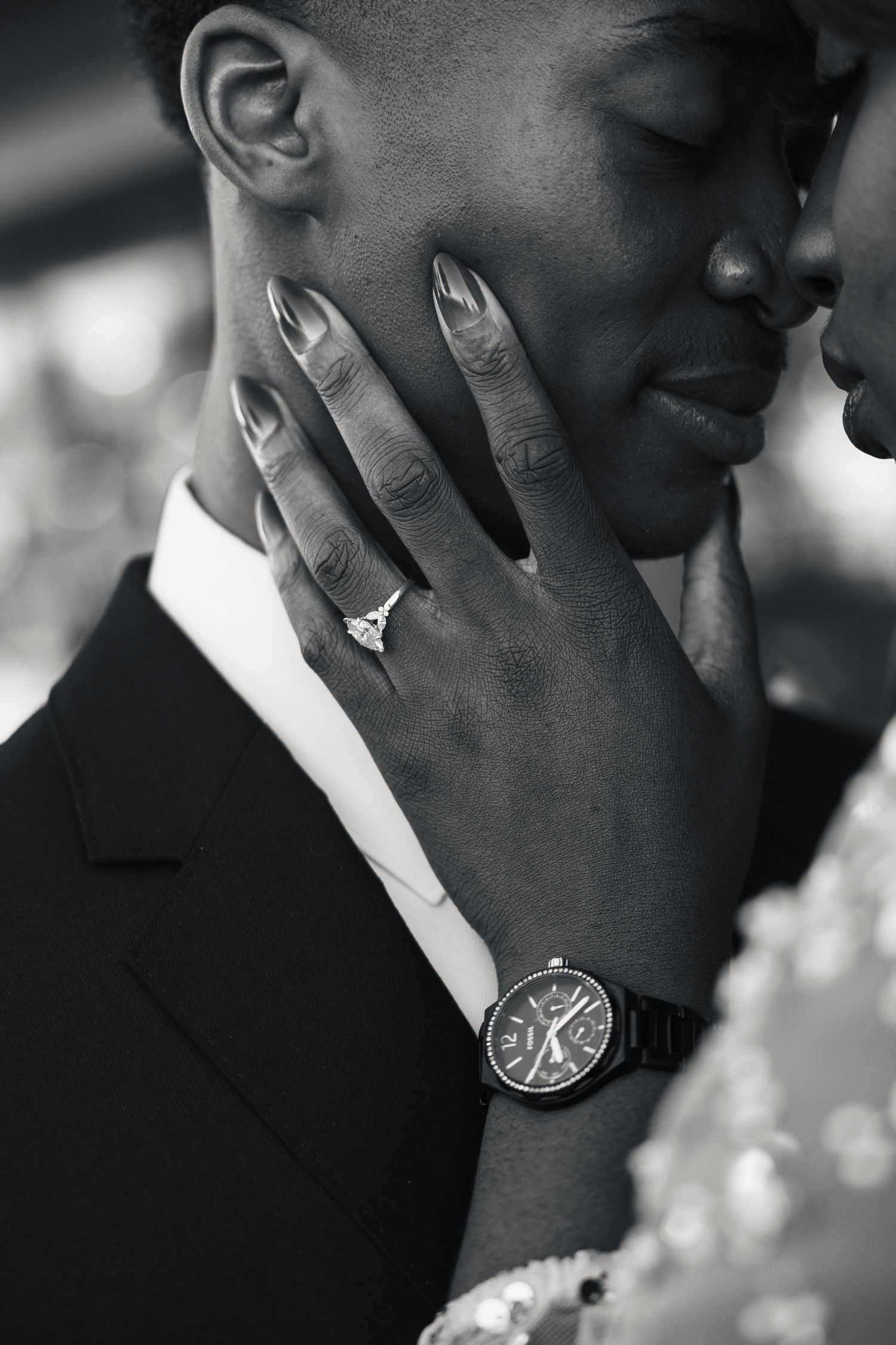 Black and white wedding photo of bride's hand with diamond ring and watch gently cradling groom's face.