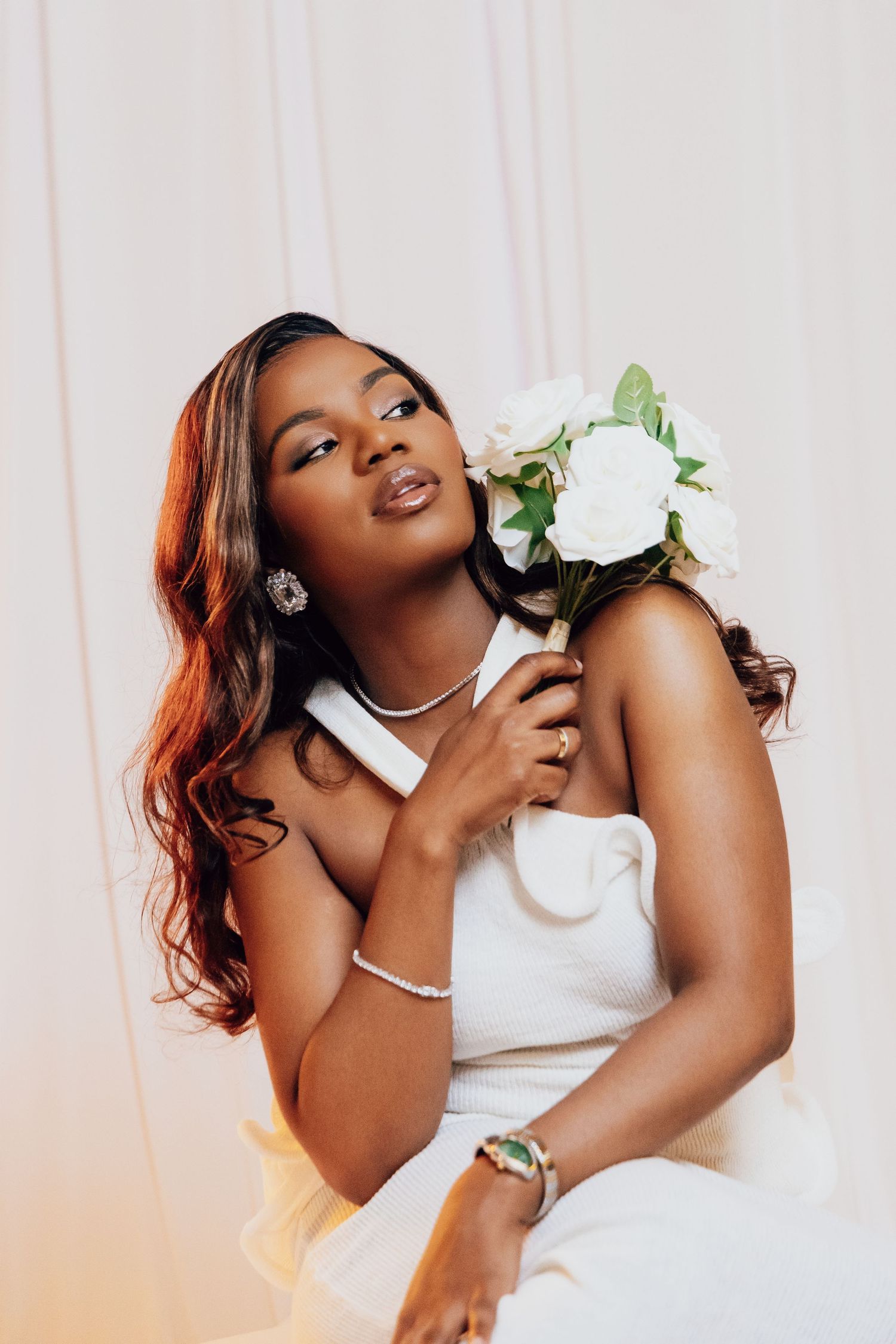 Elegant Black bride in white halter dress holding white roses bouquet, wearing diamond earrings and bracelet.
