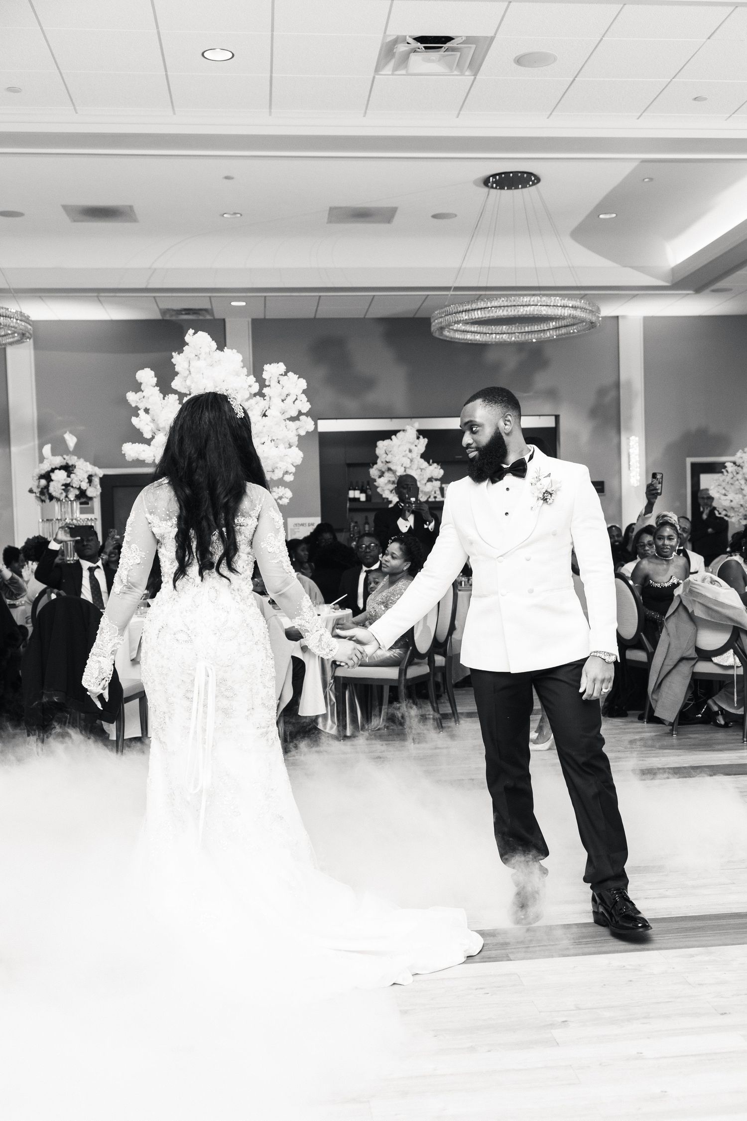 Black and white photo of bride and groom sharing first dance surrounded by dramatic fog at elegant wedding reception.