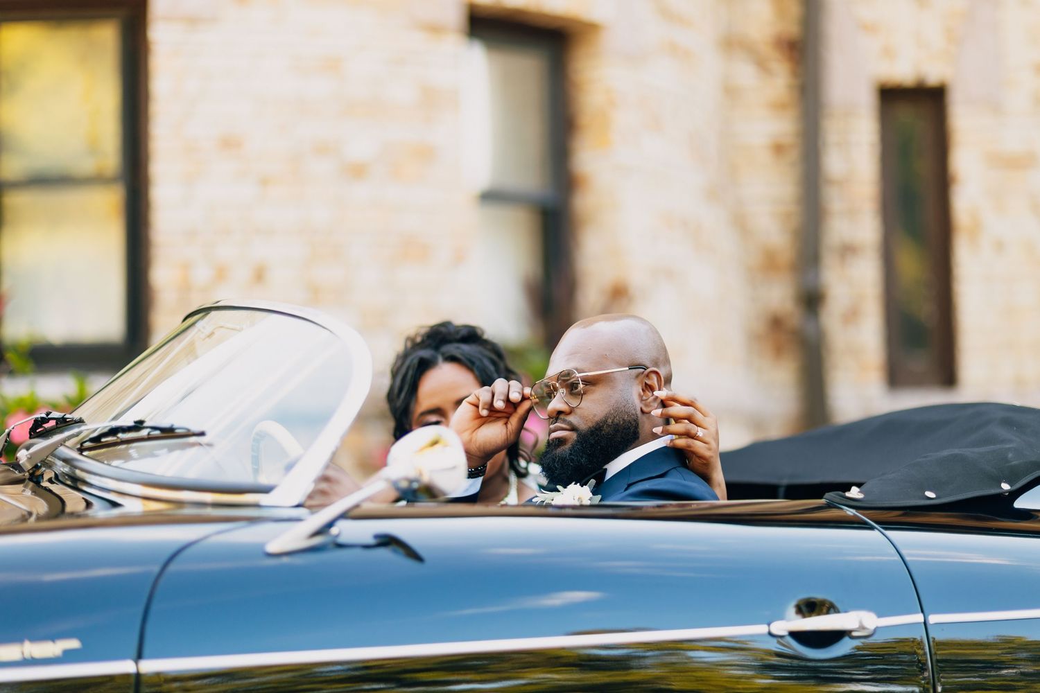 Bride and groom share a romantic moment in a classic black convertible on their wedding day.