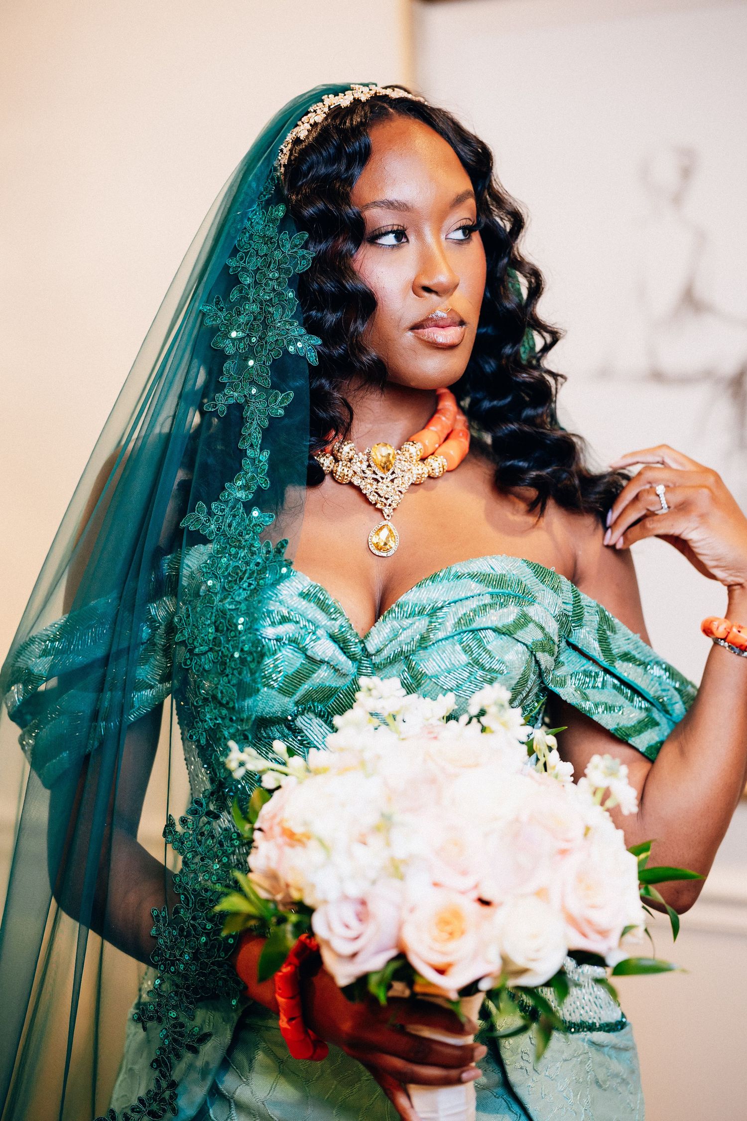 Bride in teal off-shoulder gown with lace veil, gold necklace, and bouquet.