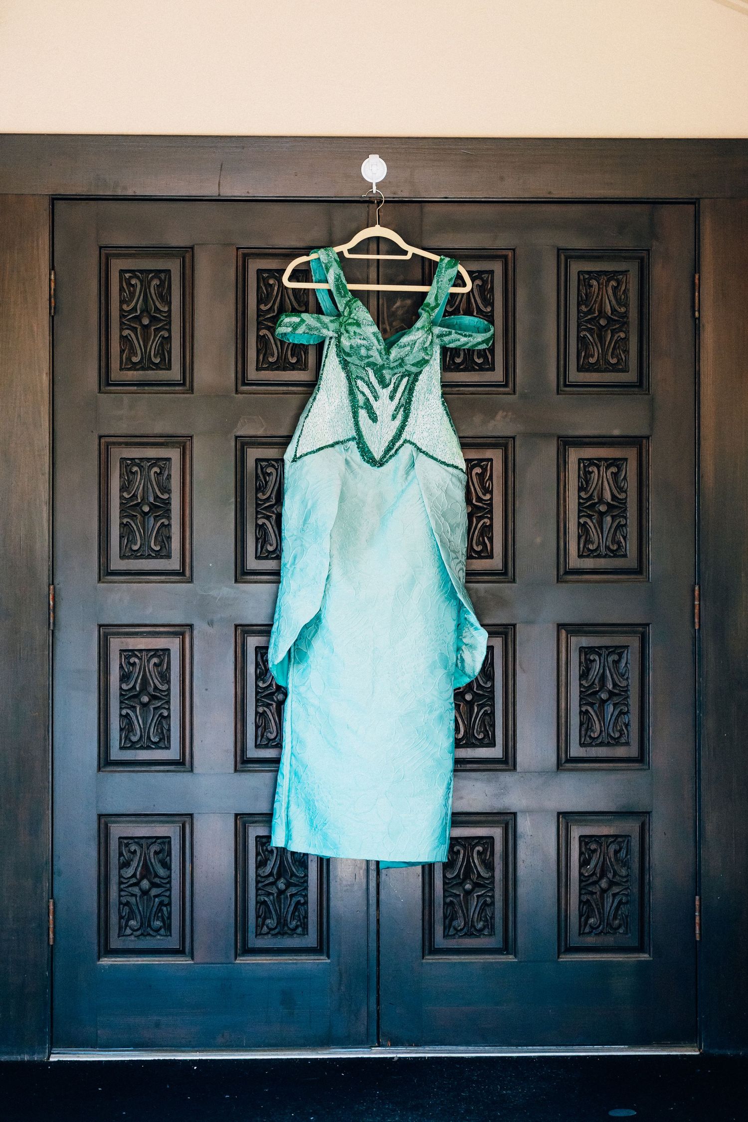 Elegant teal bridesmaid dress hanging on ornate dark wood doors on a wooden hanger.