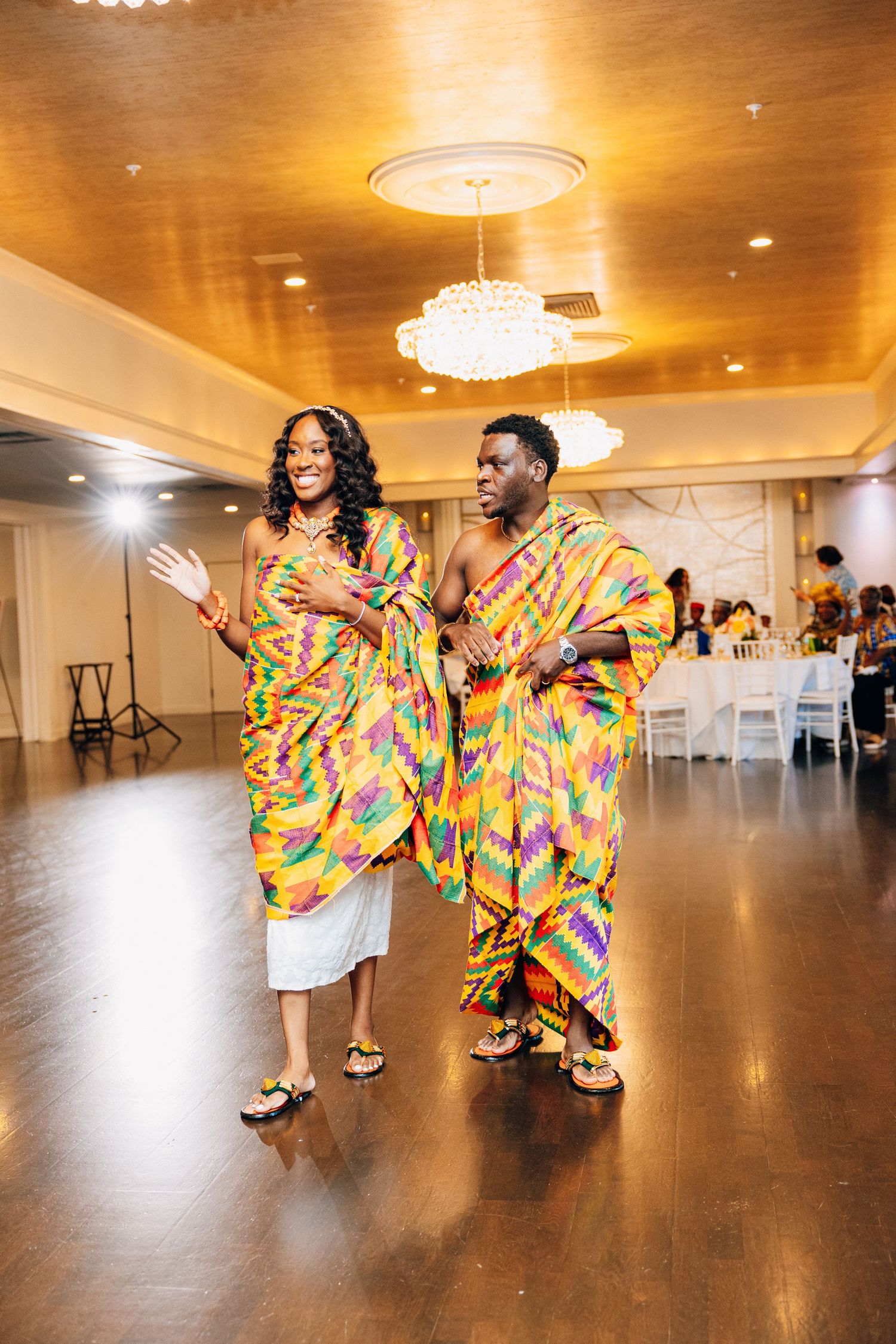 Couple in vibrant kente cloth attire dancing joyfully at a wedding reception.