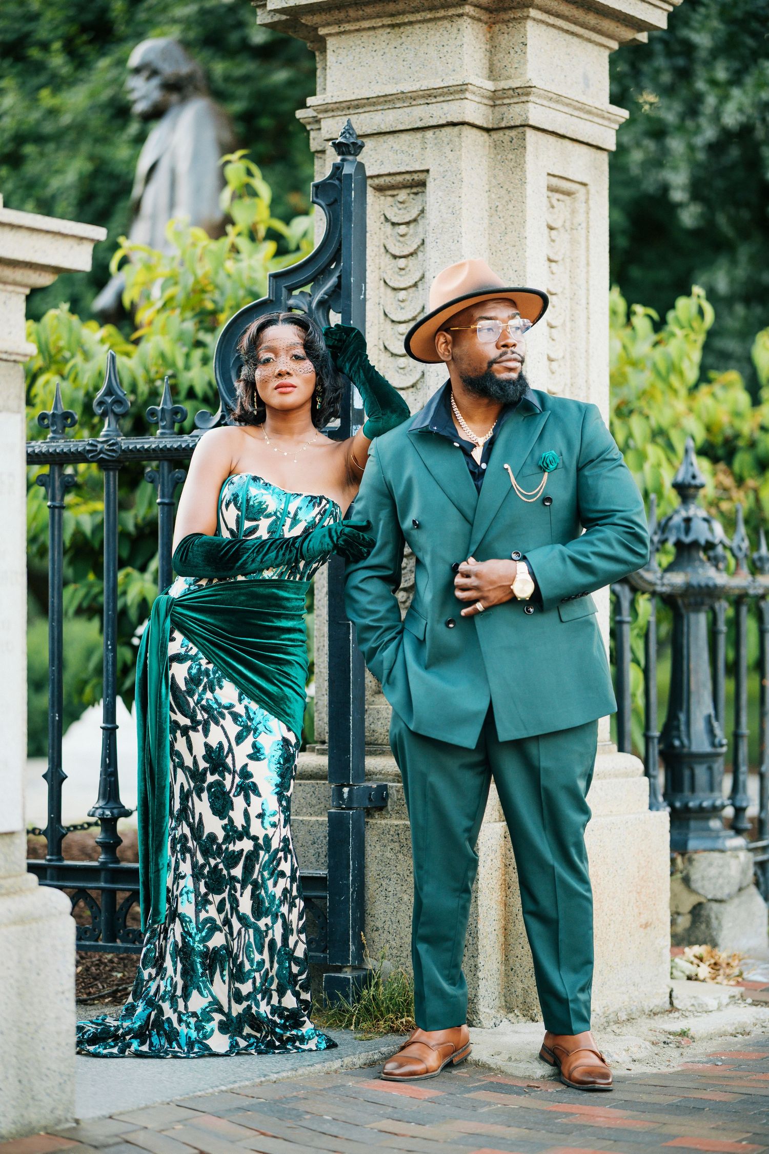 Sophisticated couple in emerald green gown and suit posing by ornate iron gate.