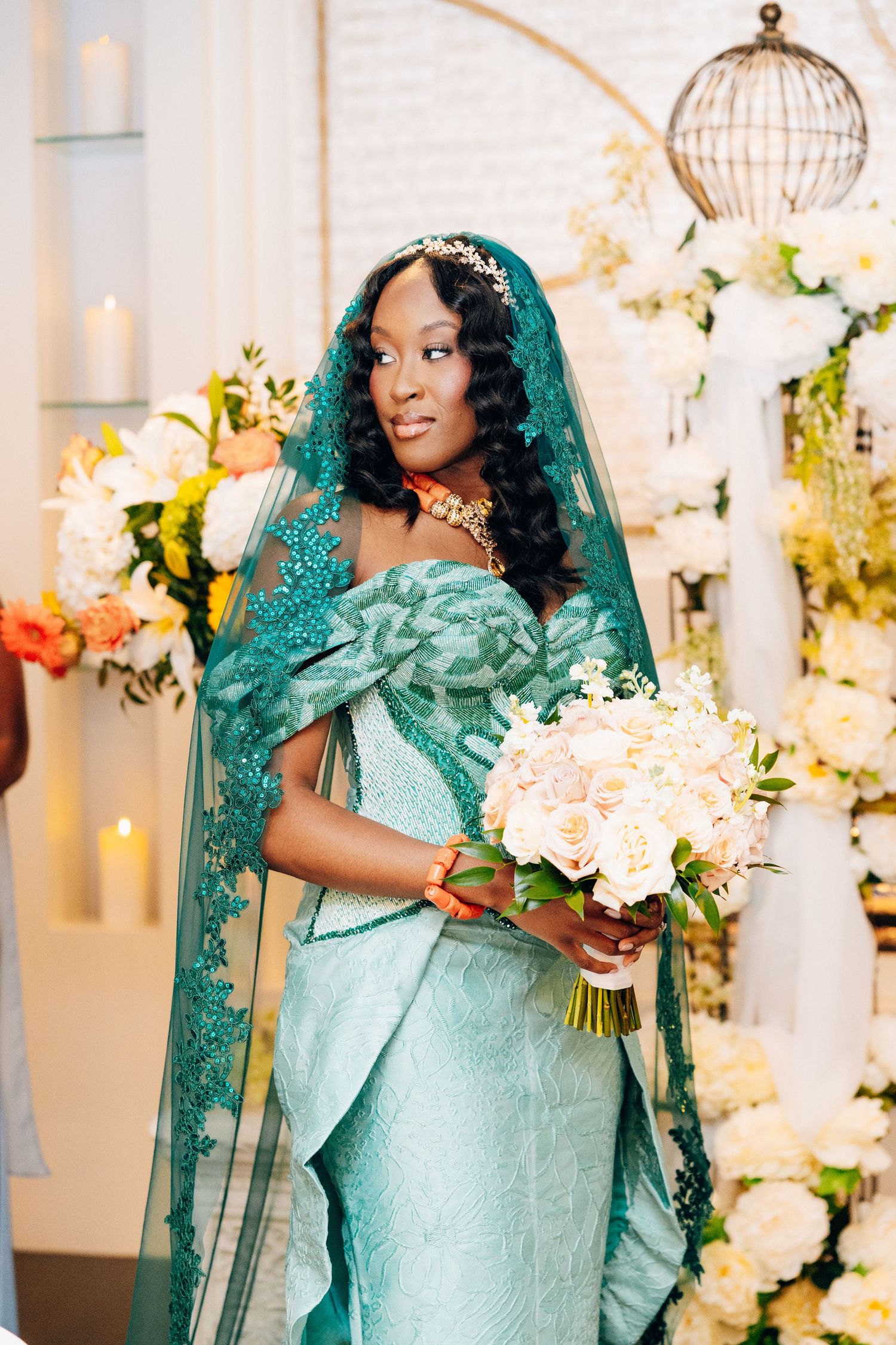 Bride in stunning teal lace gown and matching veil holding white rose bouquet.