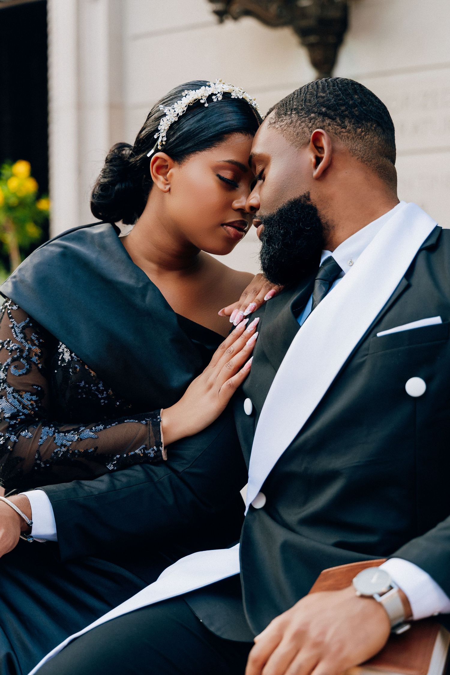 Elegant Black couple in formal attire share an intimate moment, woman in lace dress with tiara, man in black tuxedo.