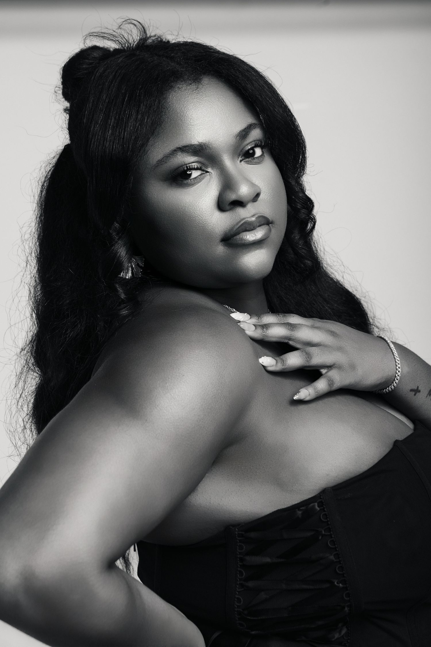 Black and white portrait of a young woman with long hair, wearing a strapless top, posing gracefully.