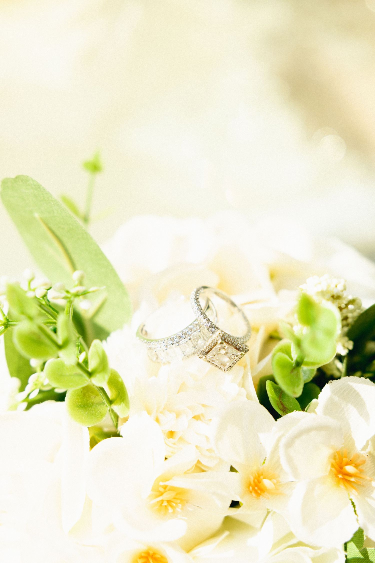 Diamond wedding rings nestled in a bridal bouquet of white orchids and green flowers.