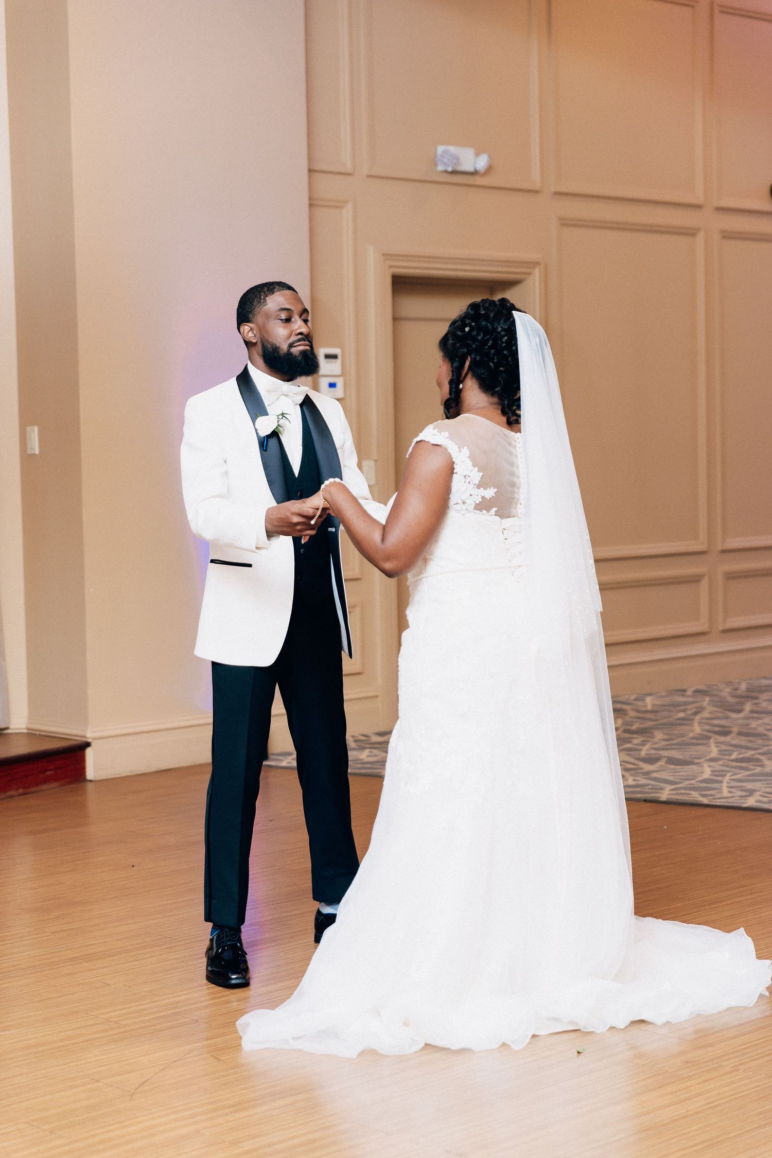 A bride and groom share their first dance in an elegant ballroom, with the bride in a lace gown and veil.