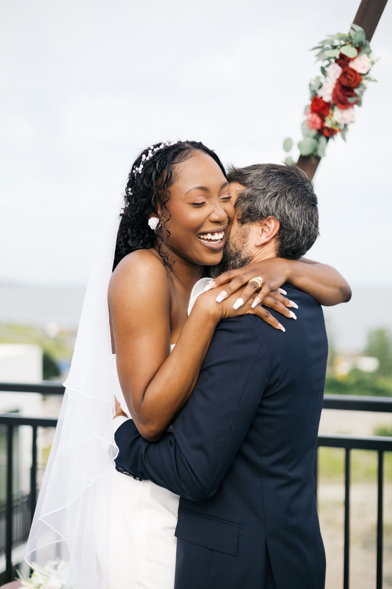 Joyful interracial bride and groom embracing and laughing after their wedding ceremony outdoors.