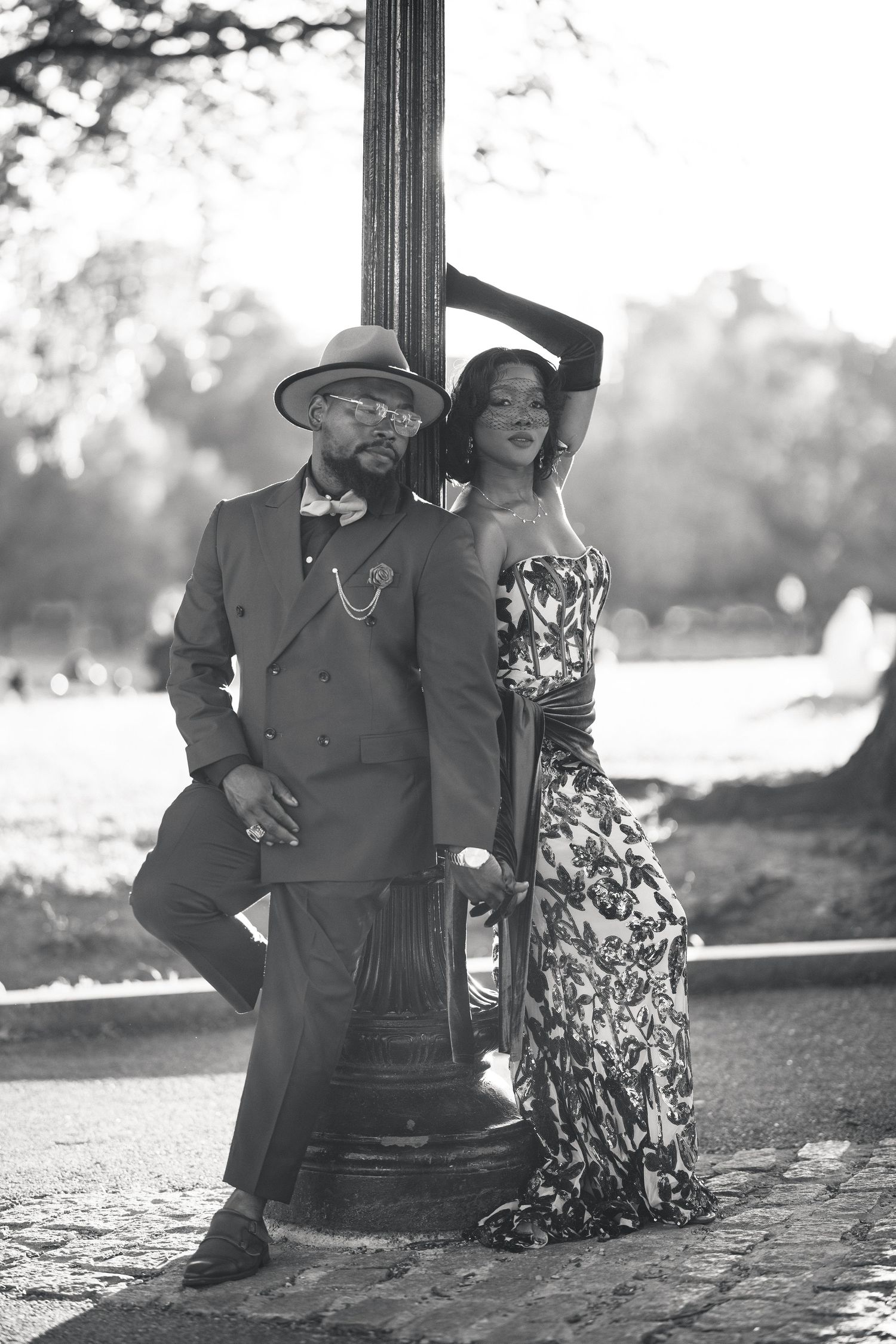 Stylish Black couple in black and white photo posing by a lamppost in a park setting.