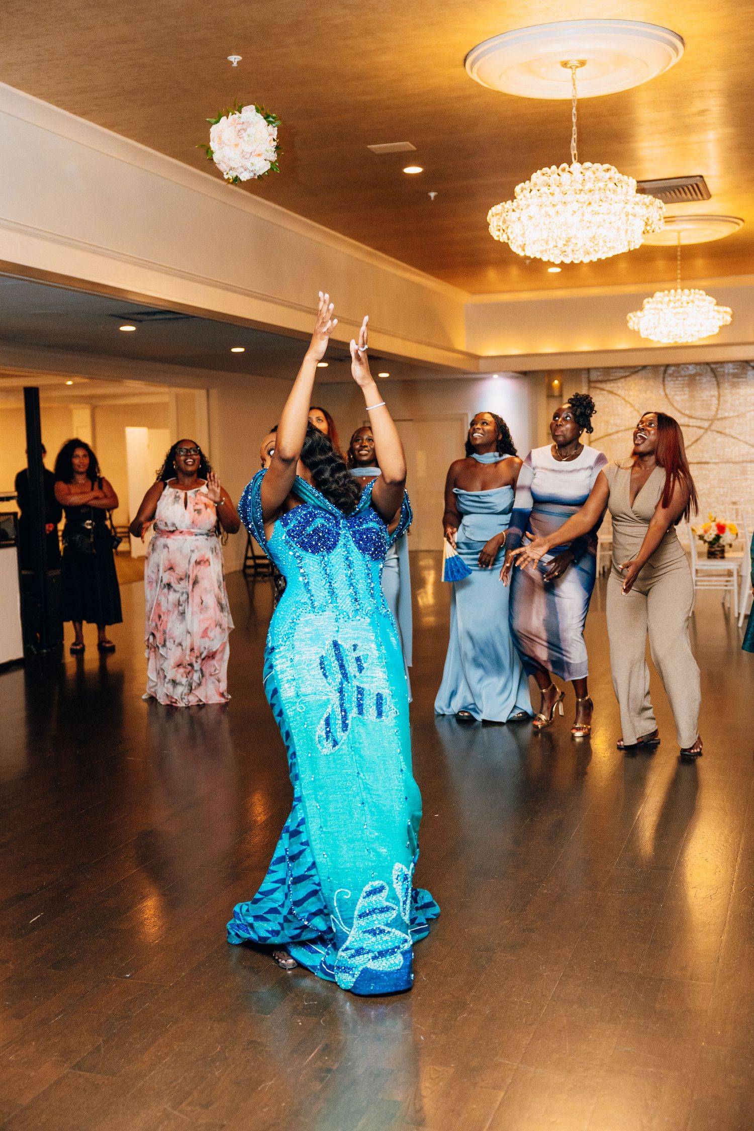 Bride in turquoise beaded gown tossing bouquet to excited guests at a wedding reception bouquet toss.