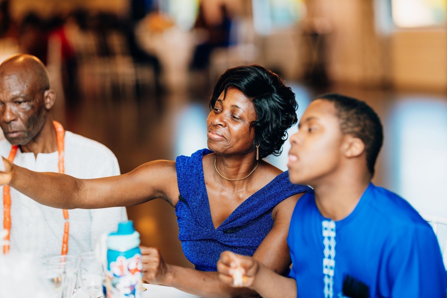 A woman in a blue dress gestures at a table during a vibrant African wedding reception celebration.